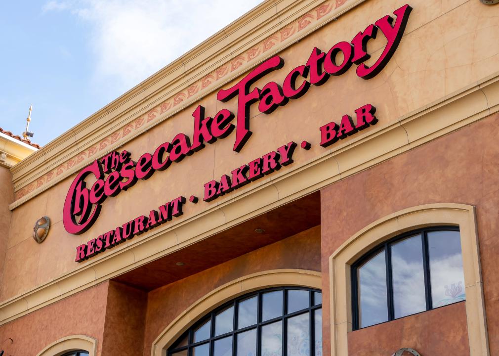 A close up of The Cheesecake Factory sign on a building with the words restaurant, bakery, bar underneath it. 