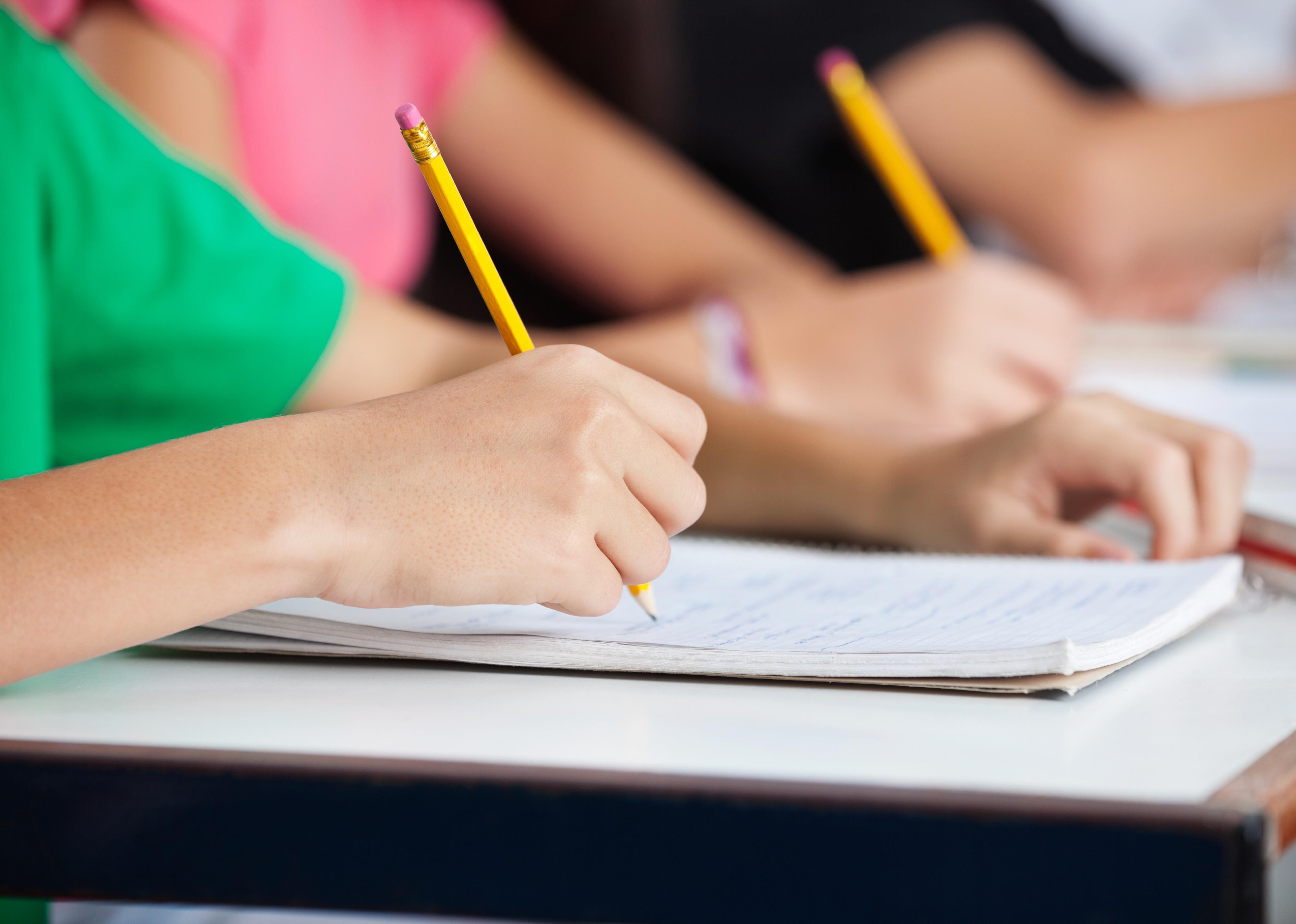 Midsection of teenage classmates writing in book at desk