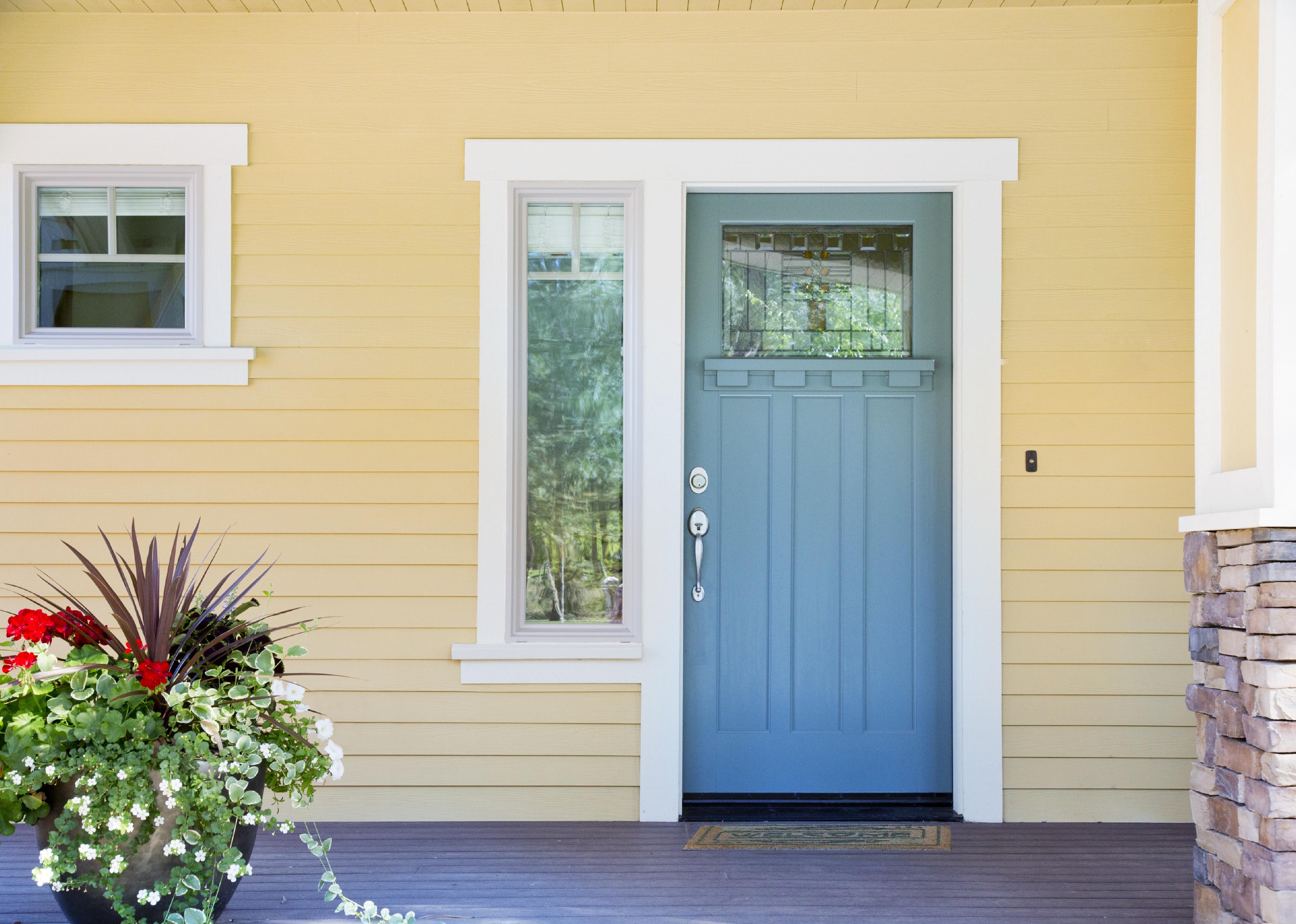 A front entrance of a home with a blue door, yellow siding, and a flowerpot.