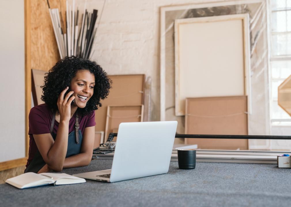 Young female artisan working on laptop and talking on the phone