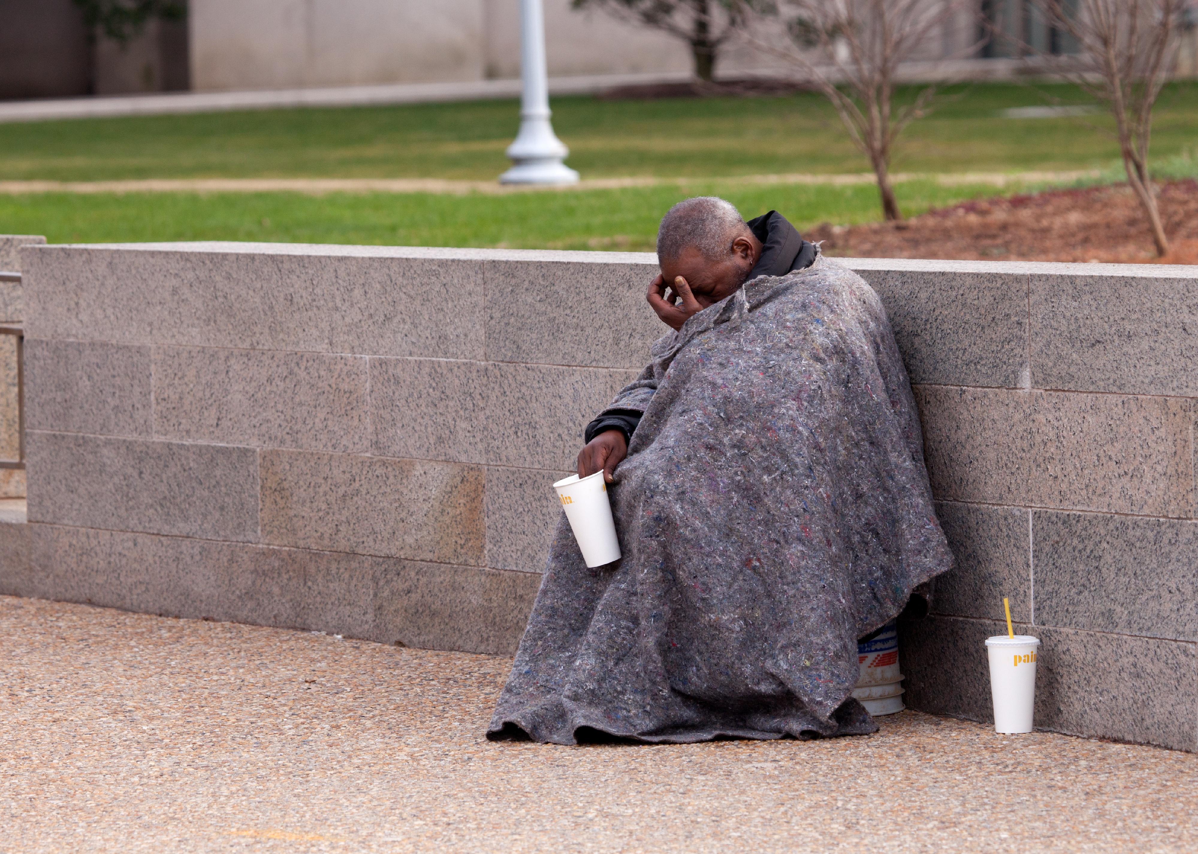 Homeless man hangs his head while sitting on the street try to collect money.