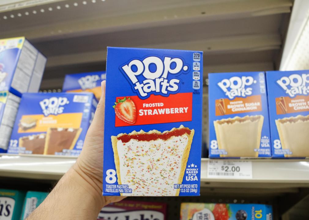 A view of a hand holding a box of Pop Tarts Frosted Strawberry.