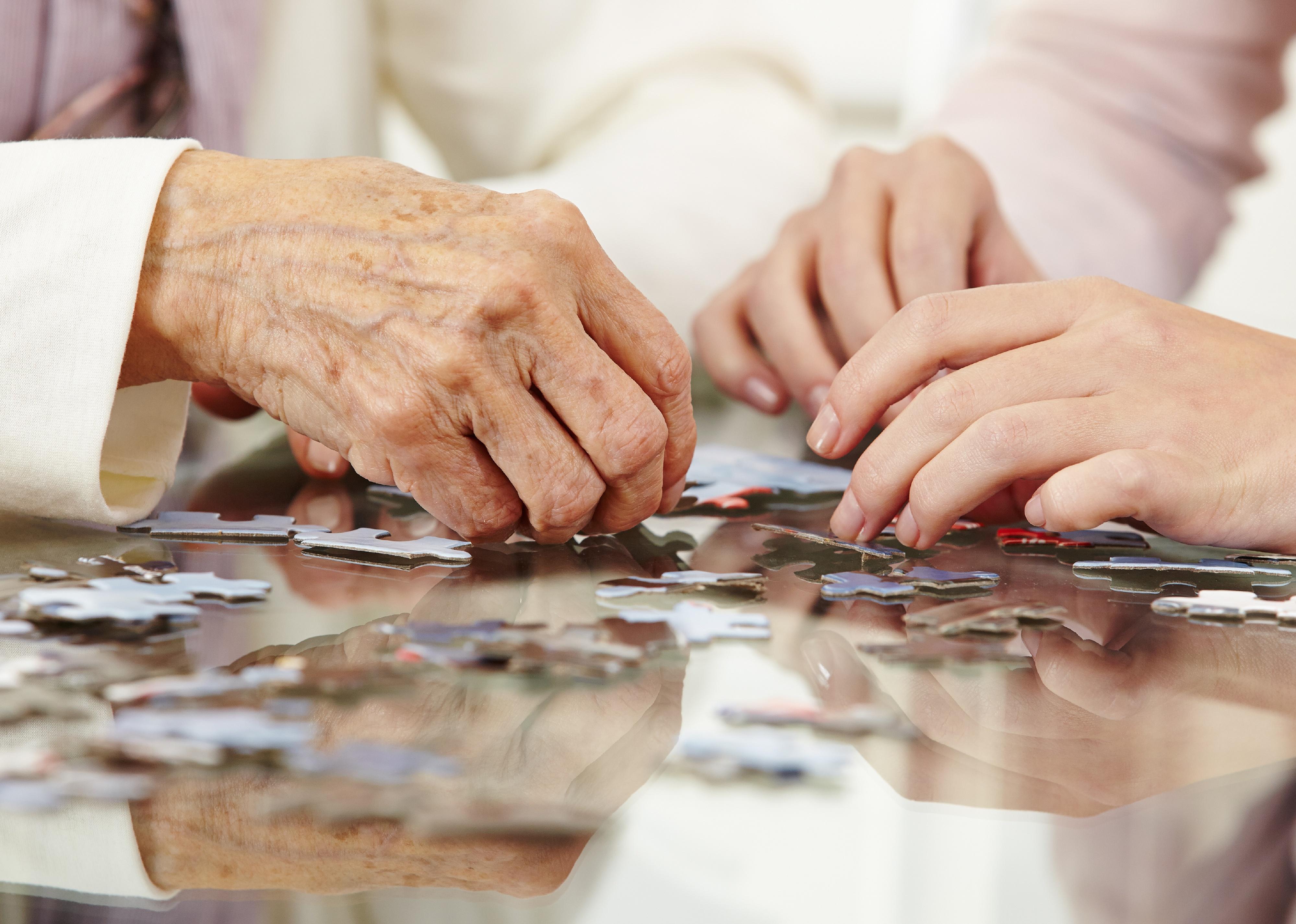 Elderly hands and younger hands solving a jigsaw puzzle together.