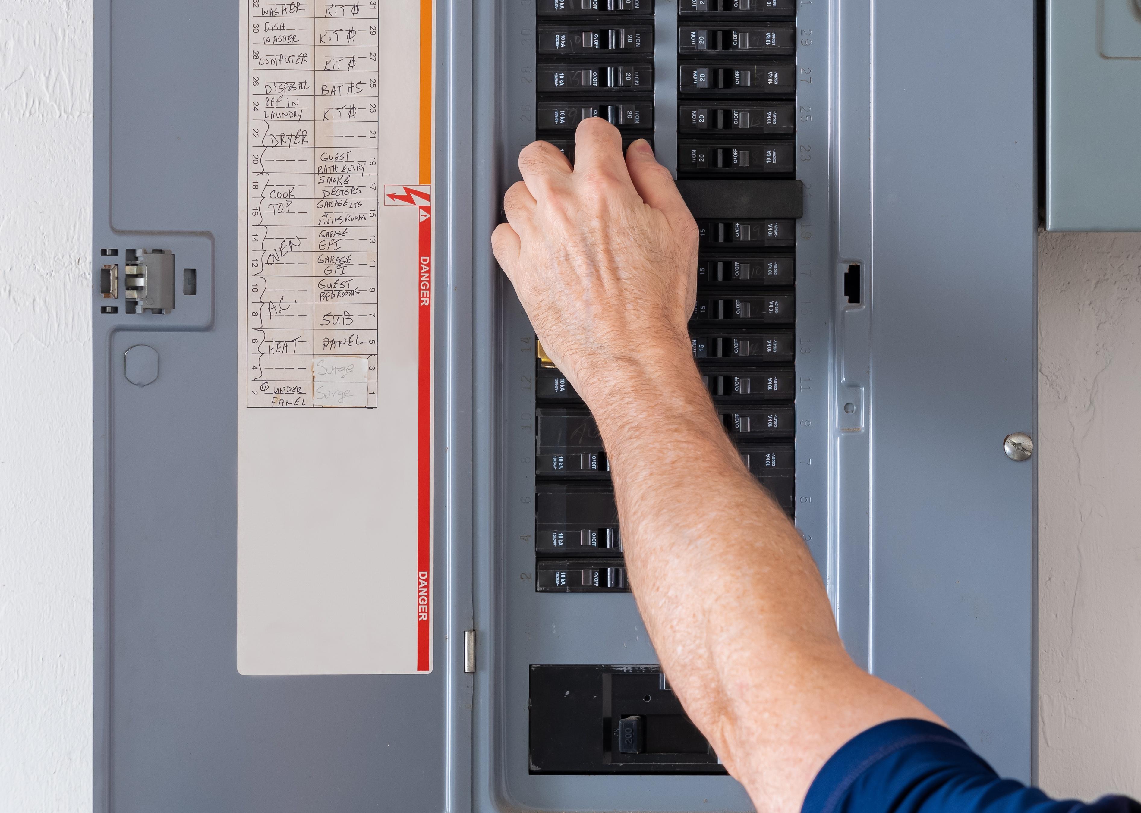 Electrician turning off power for electrical outlet at circuit breaker box.