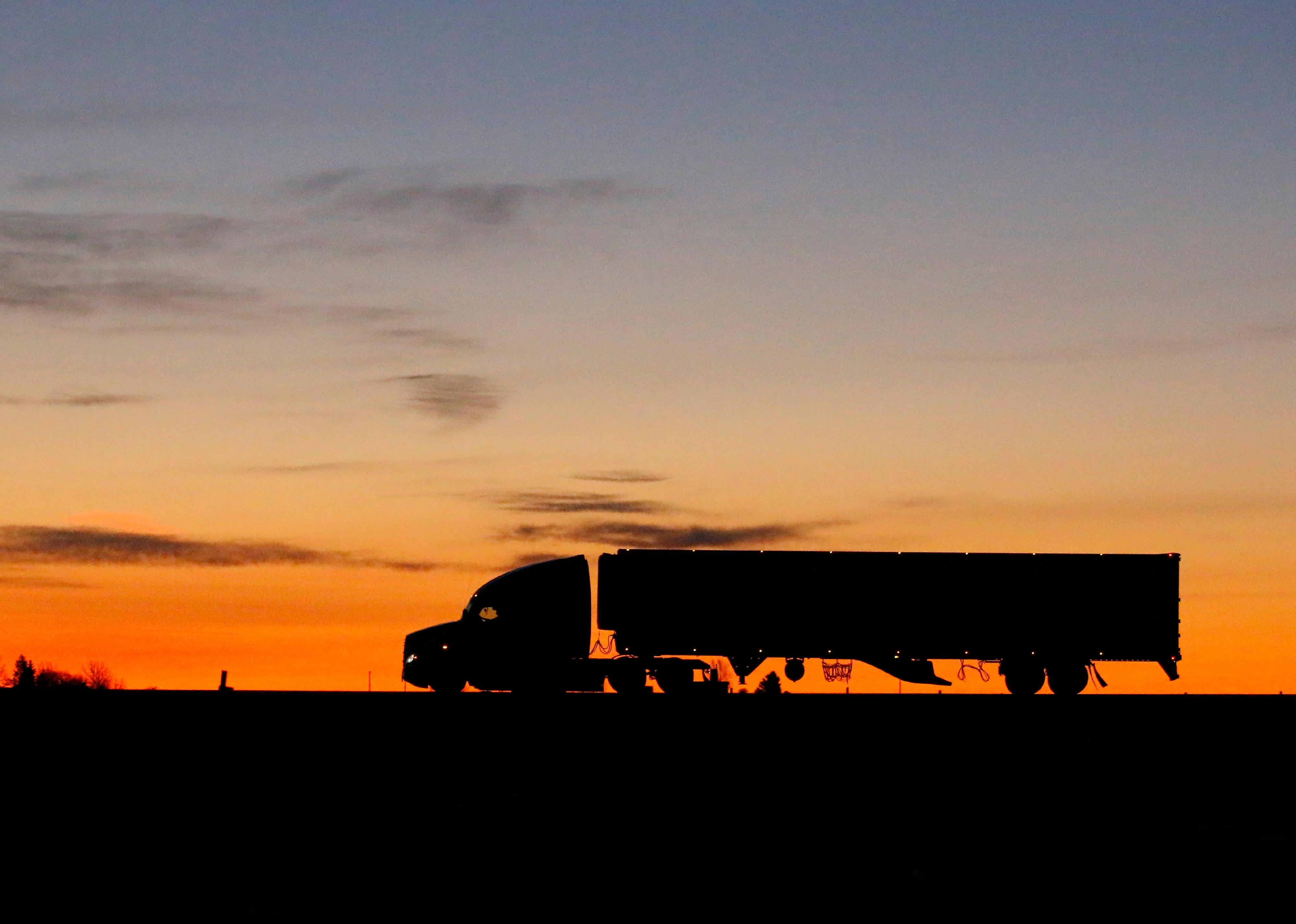 Silhouette of a large truck driving on a road at sunrise.