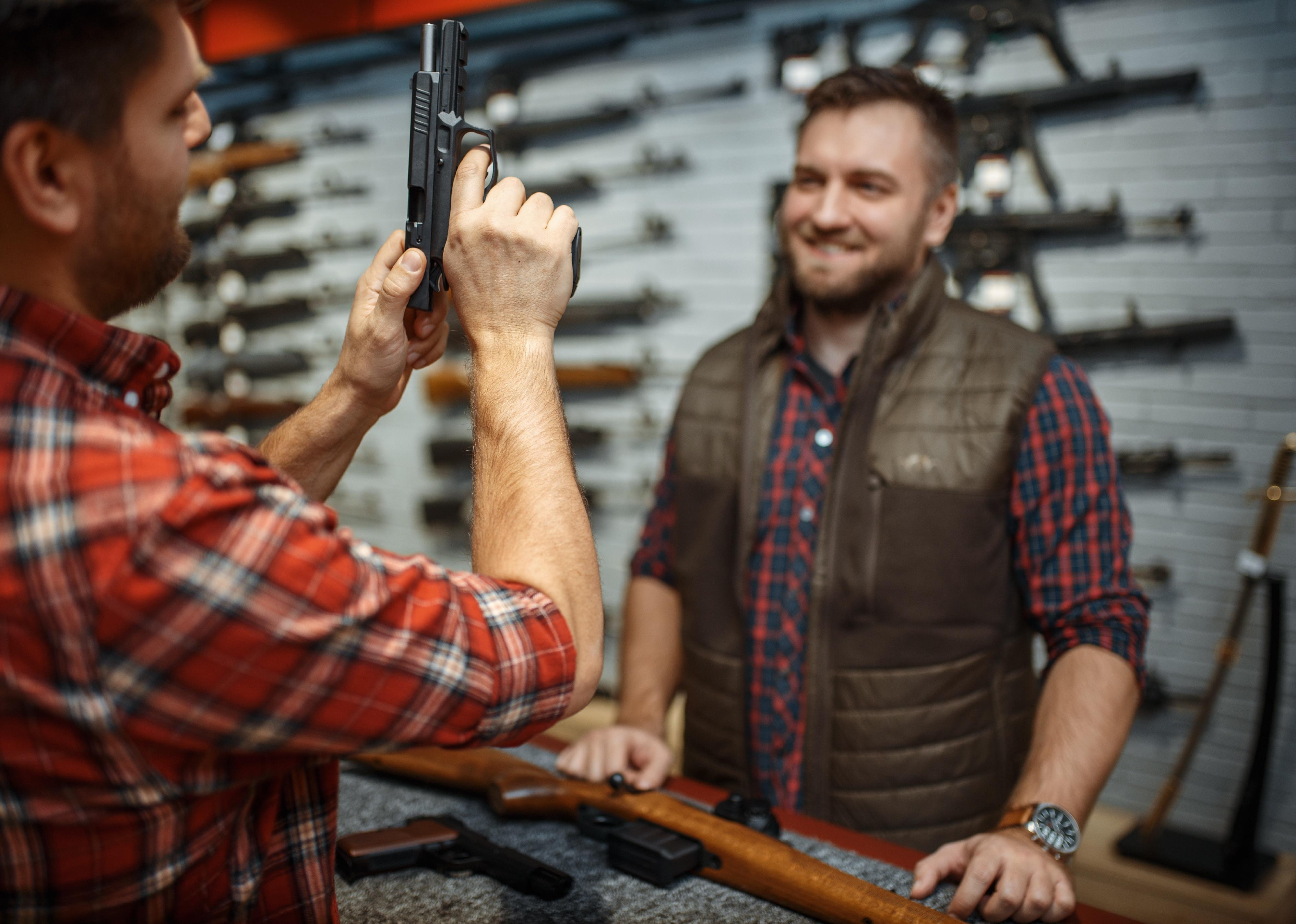 Person with store owner choosing handgun in gun shop.