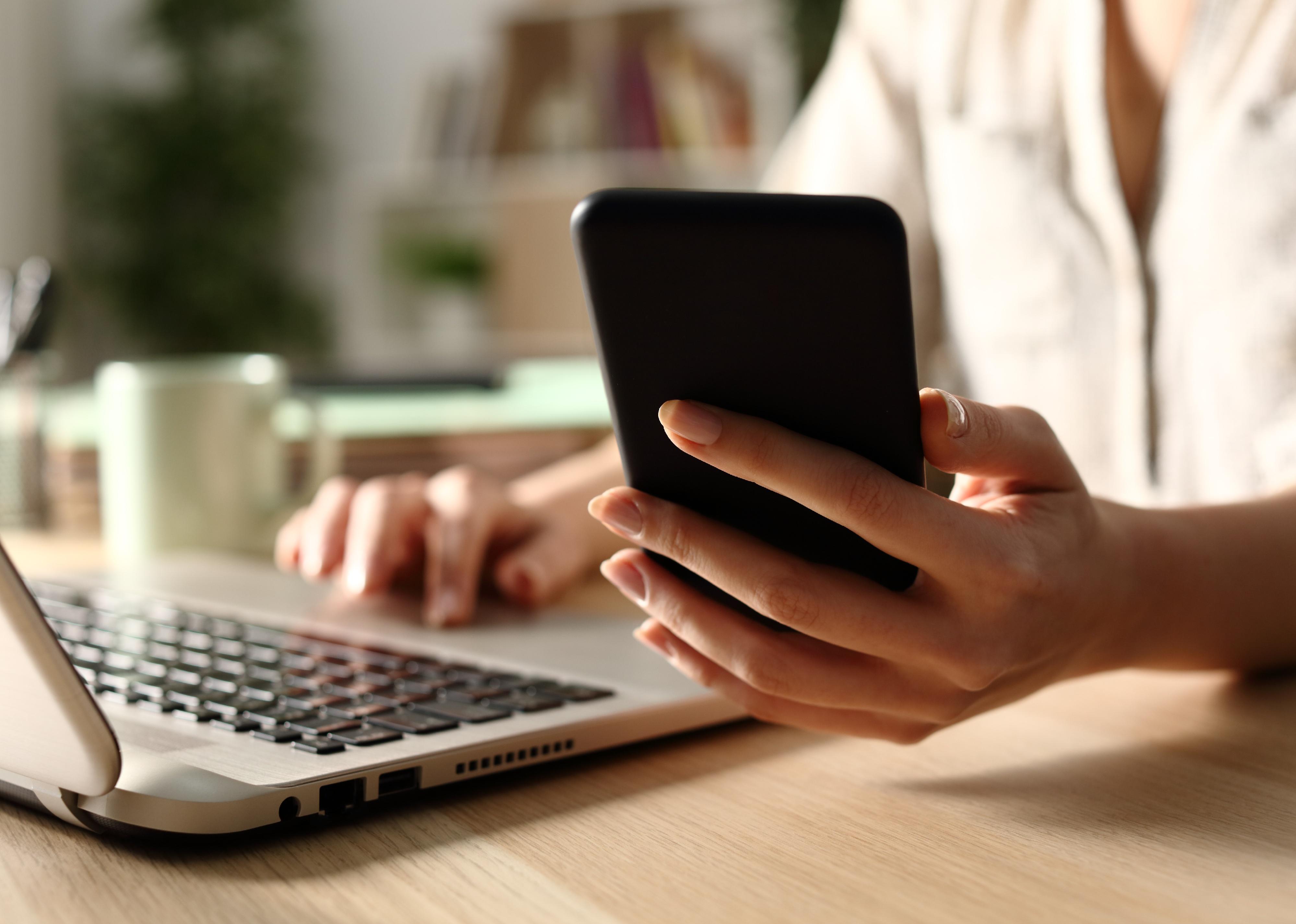 Close-up of a hands using laptop checking smartphone.