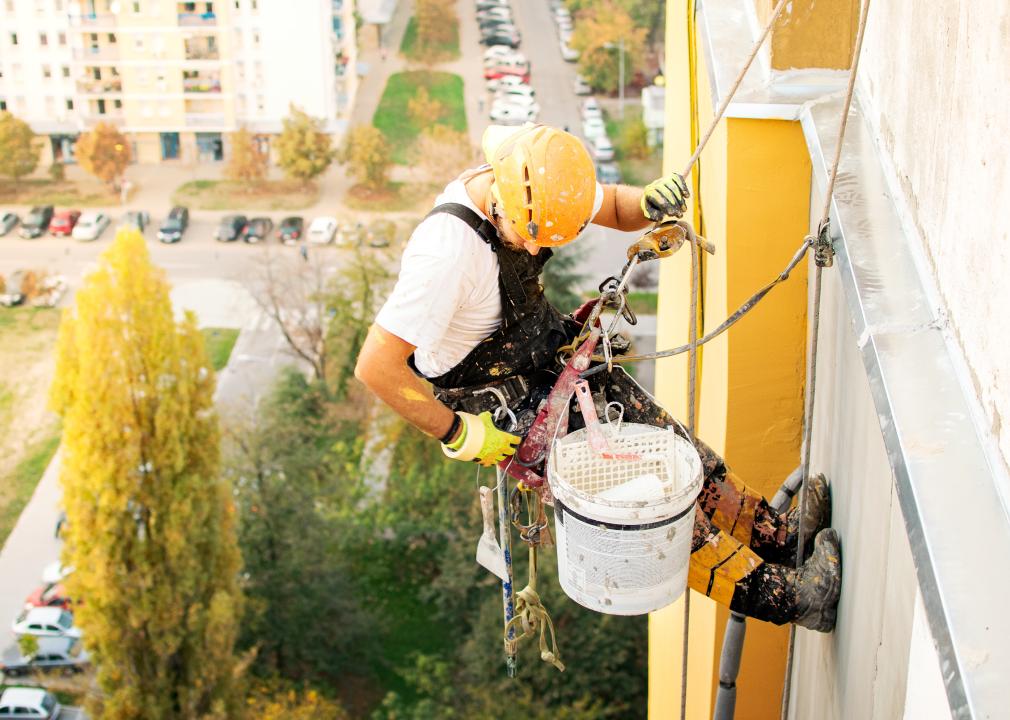 Industrial climber hanging on rope while painting a tall building