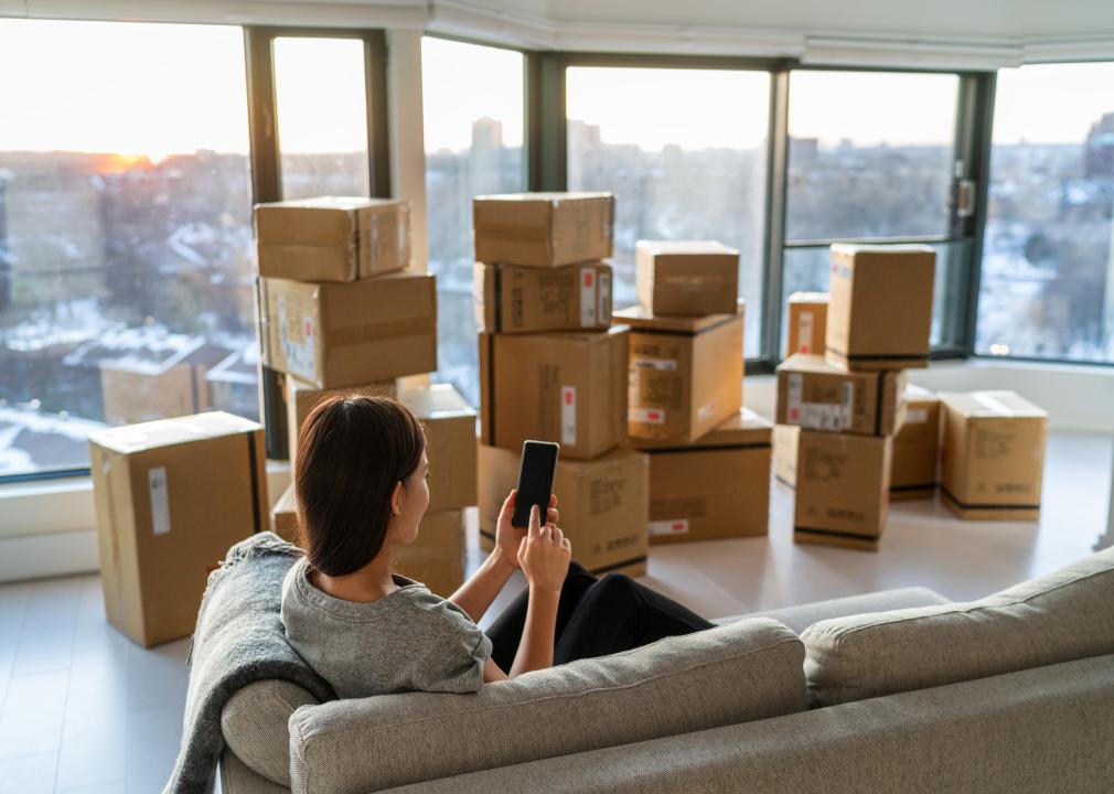 Young woman sitting on couch using phone with moving boxes