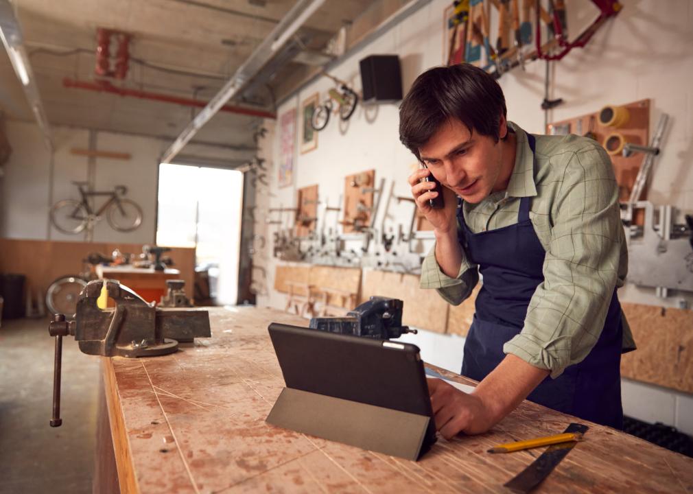 Male Business Owner In Workshop Using Digital Tablet And Making Call