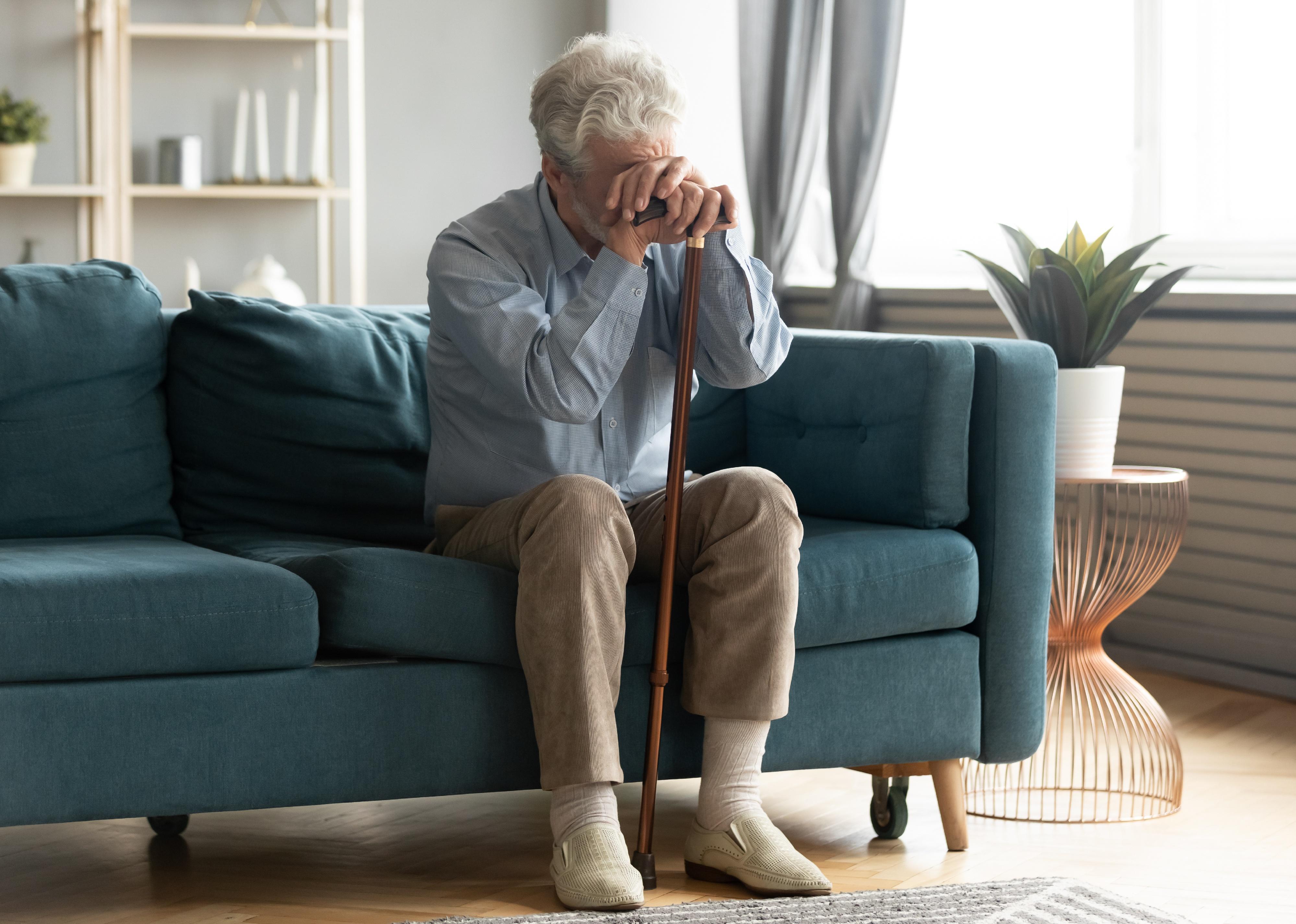 Older man resting on sofa, leaning on walking cane.
