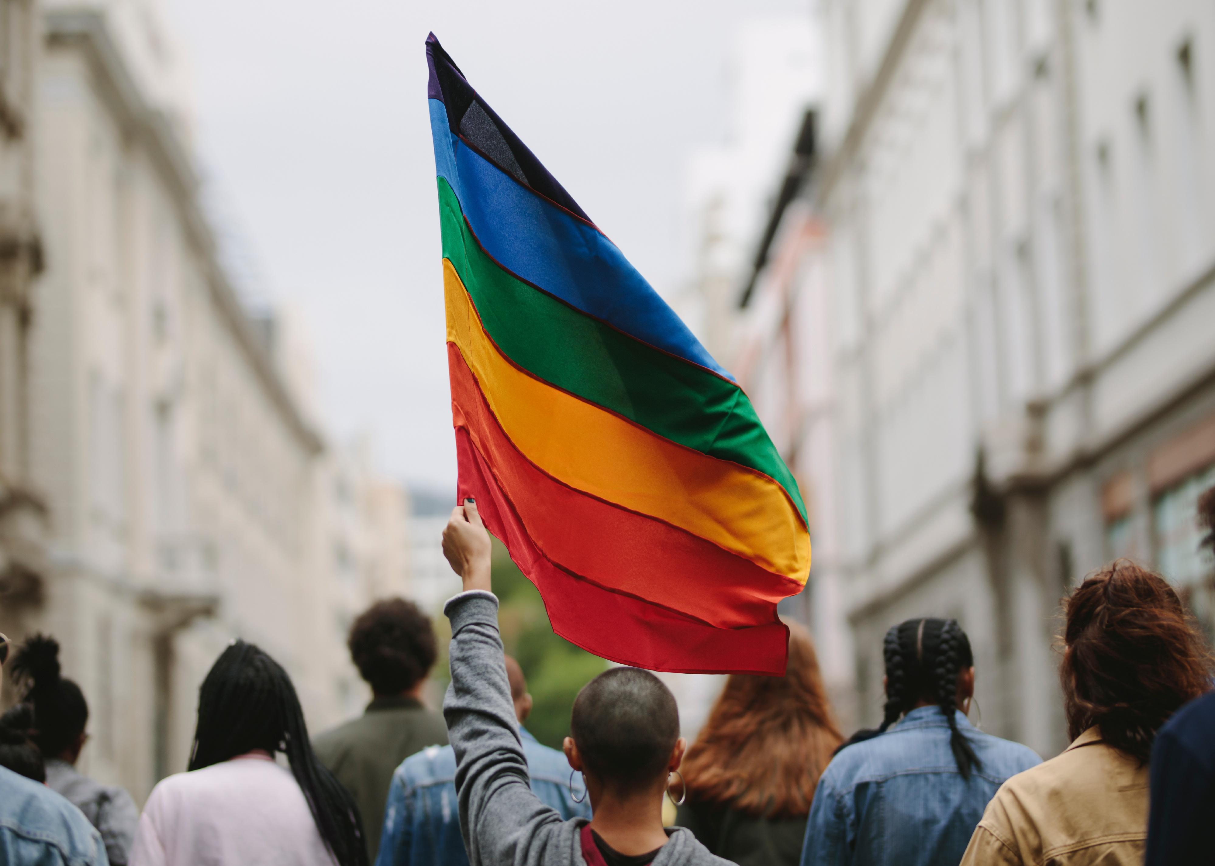 Group of people on a city street with rainbow flag.