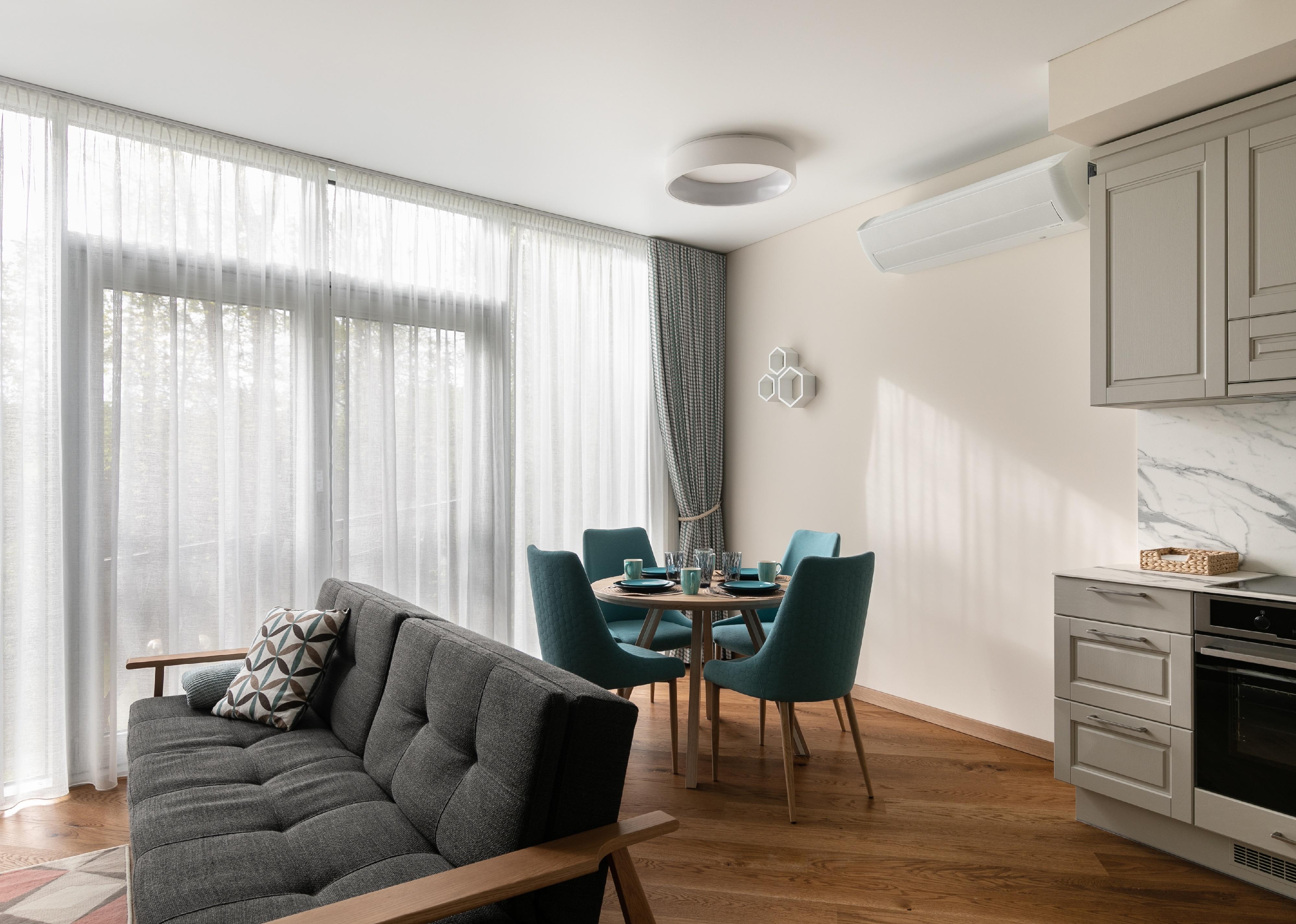 Living room in a small apartment furnished with gray sofa, round table and blue chairs.