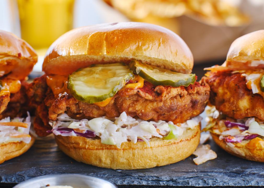 Three Nashville hot chicken sandwiches with coleslaw and pickles on the sandwiches.