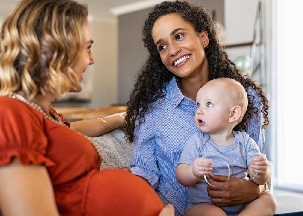 Mixed race woman with expecting mother talking and playing with baby