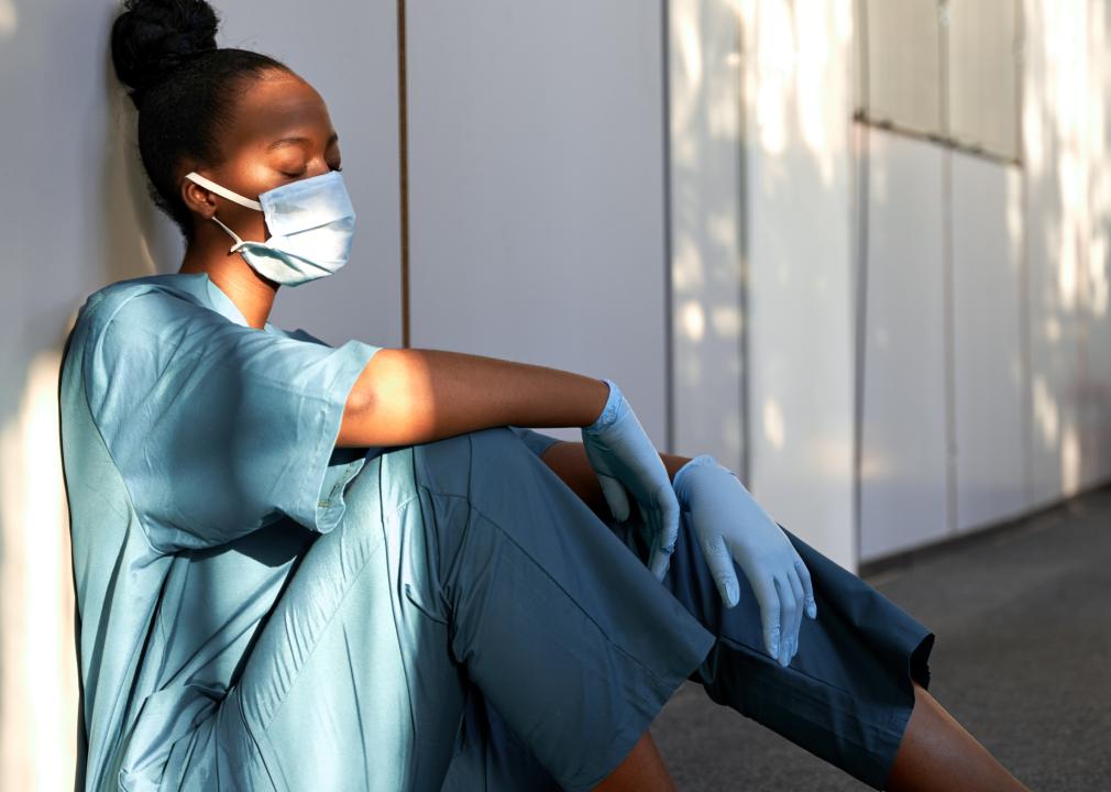 Tired female nurse with face mask sits on hospital floor