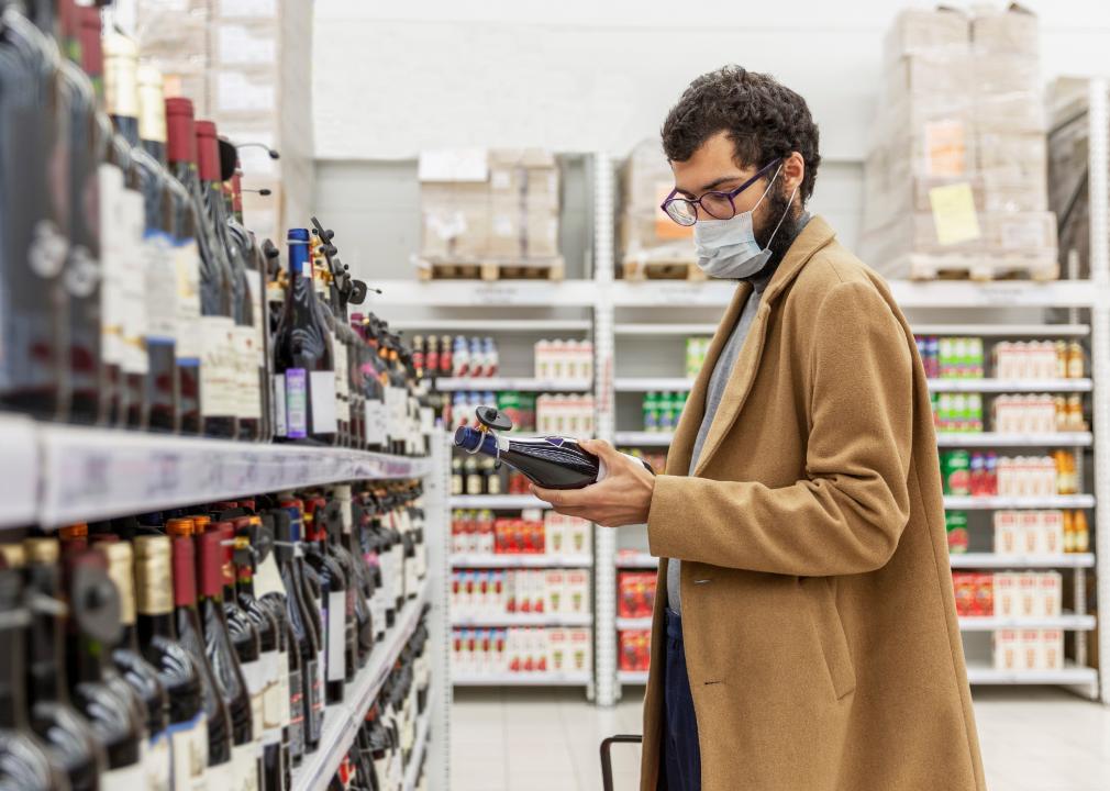 A young man in a supermarket chooses alcohol in the wine section.