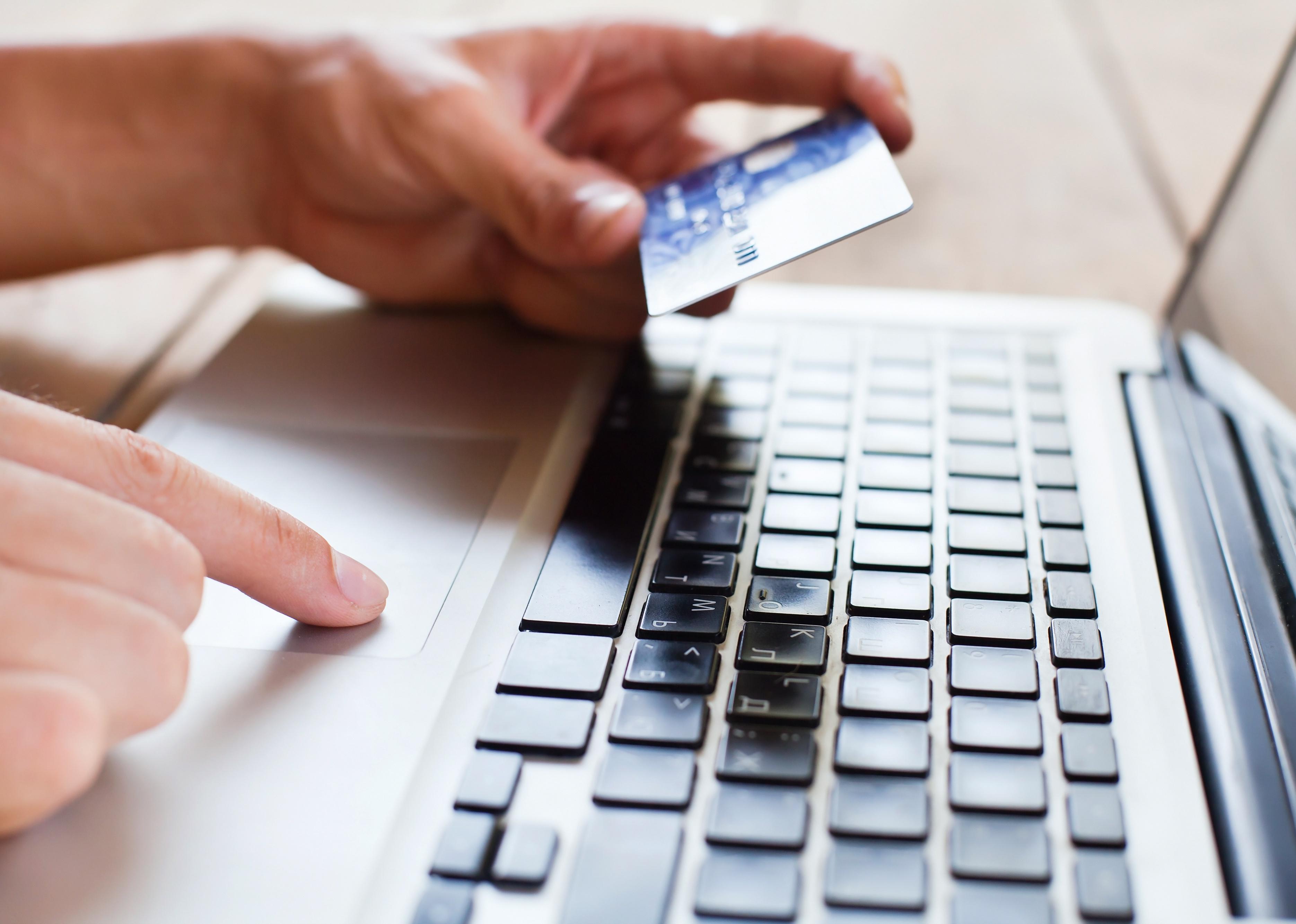 Close-up of a hand holding a credit card and typing on laptop