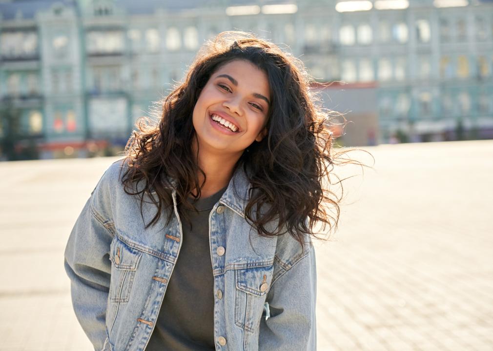 Happy young woman wearing denim jacket laughing on street.