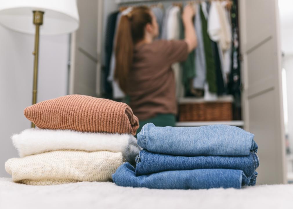 A woman organizes her closet with folded clothes stacked in the foreground.