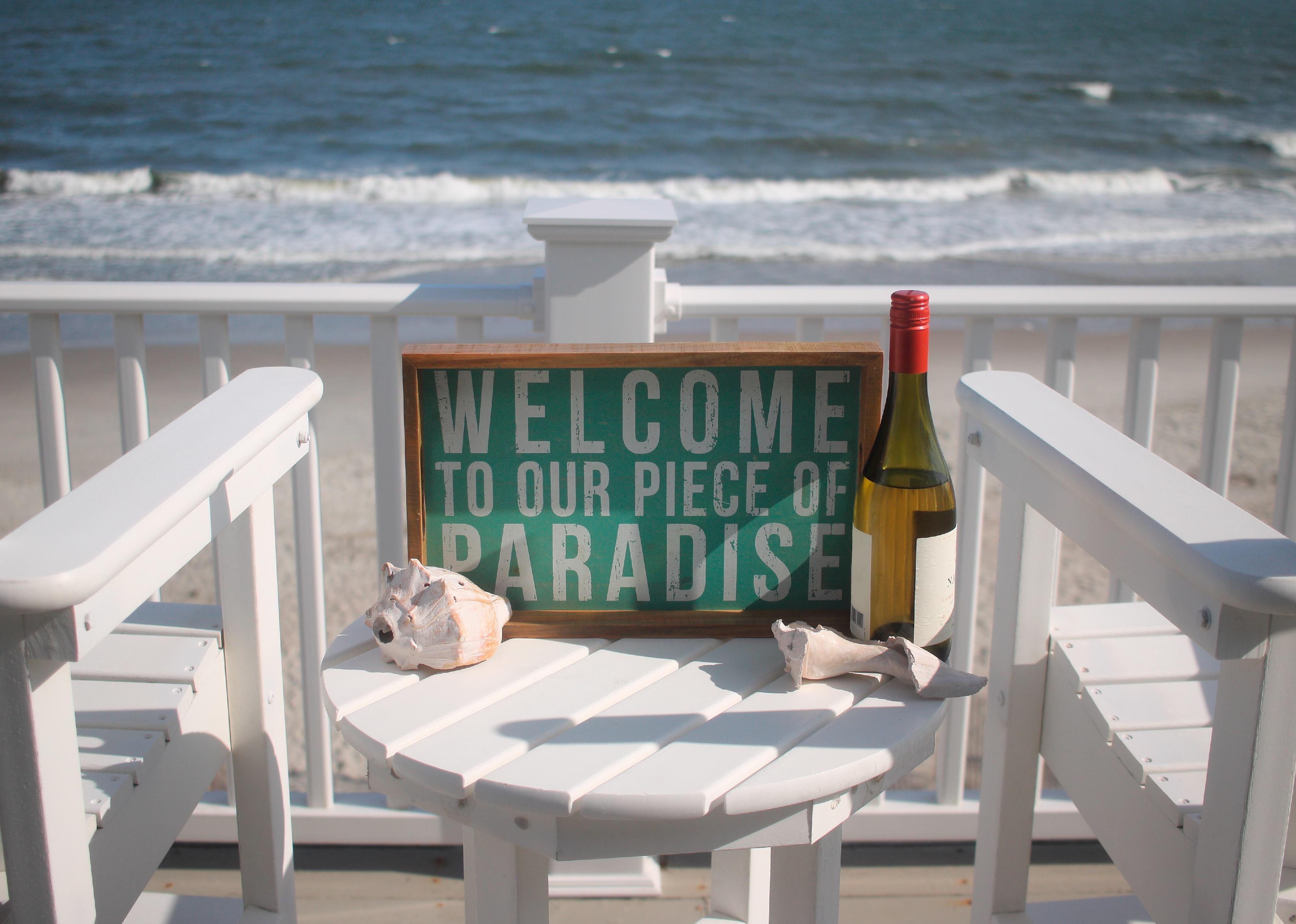 Beach house porch overlooking ocean with two chairs and paradise sign.