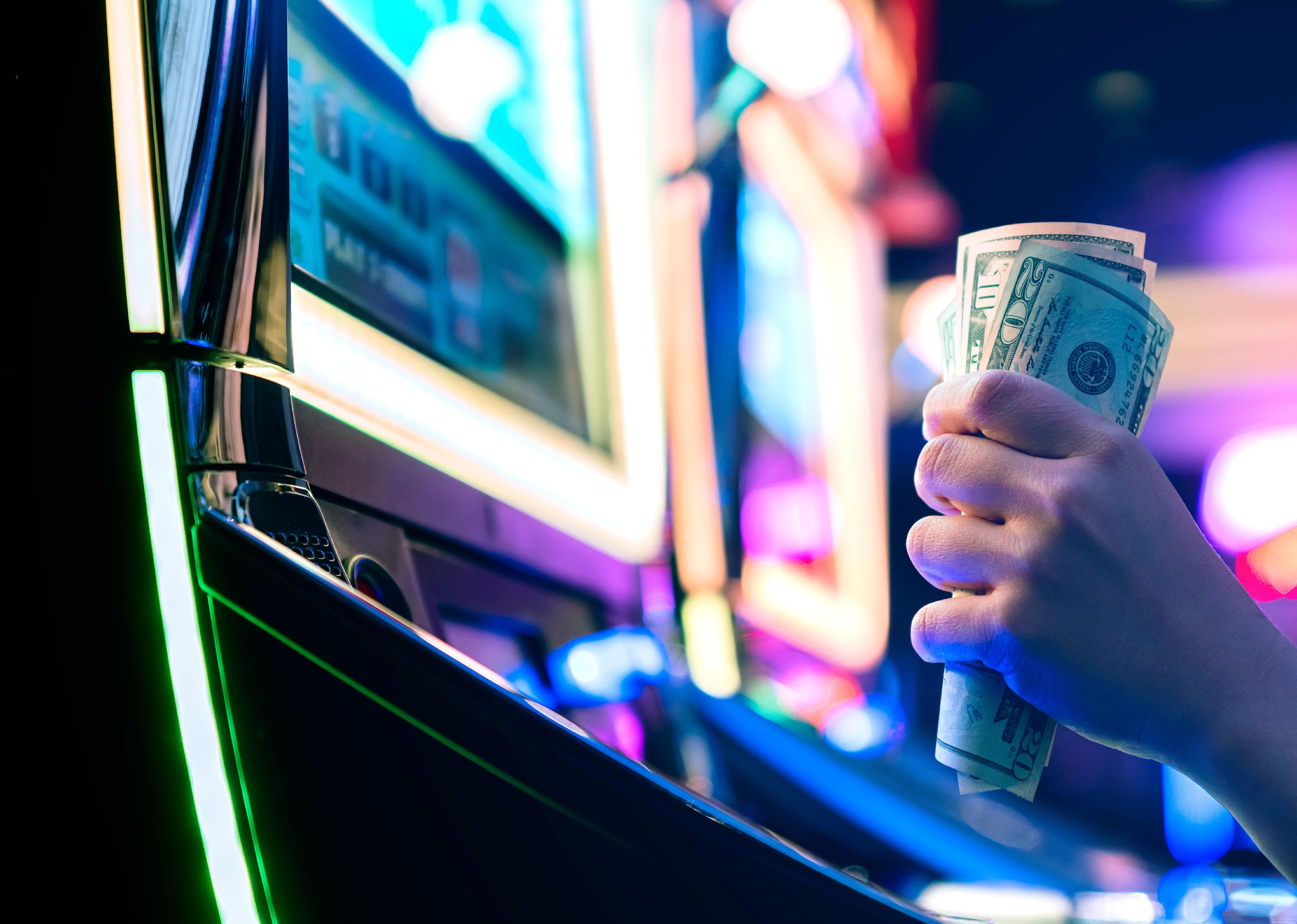 A hand holding money at slot machine.