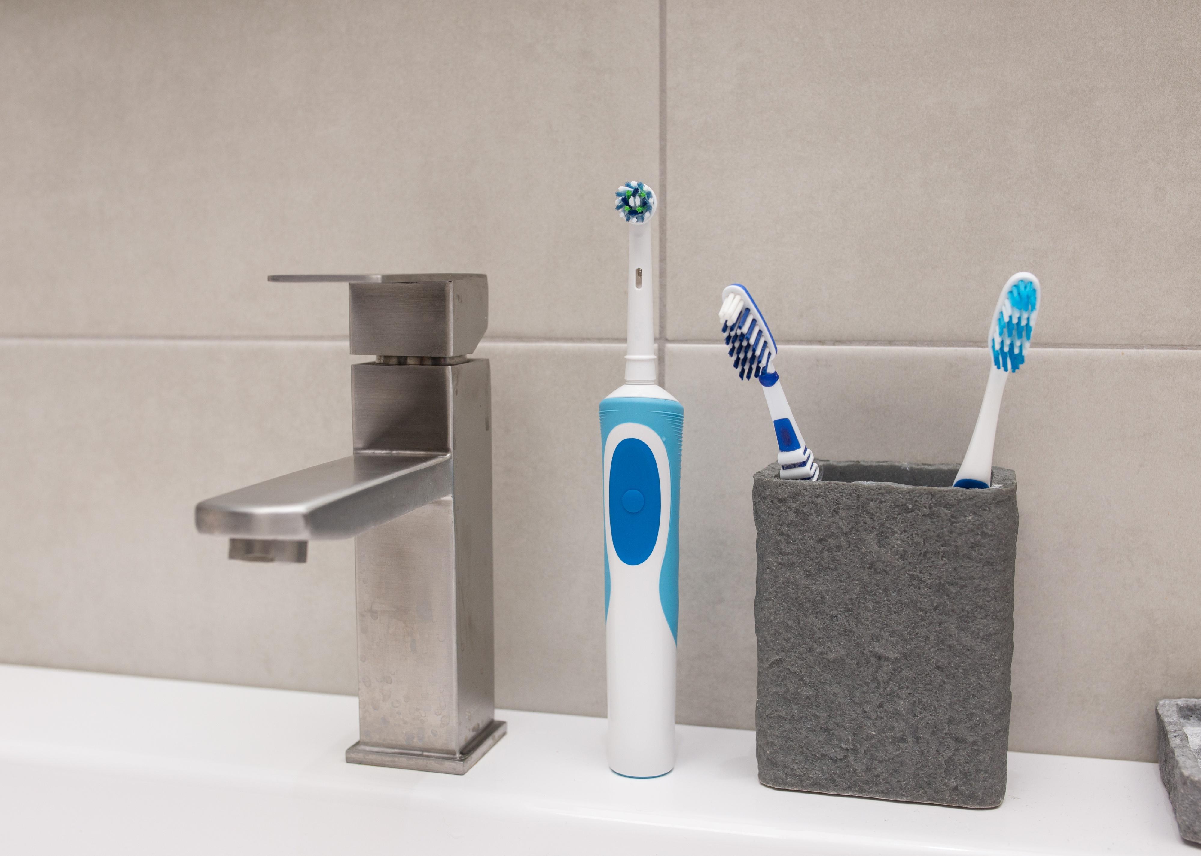 An electric toothbrush and an old toothbrush near the washbasin.