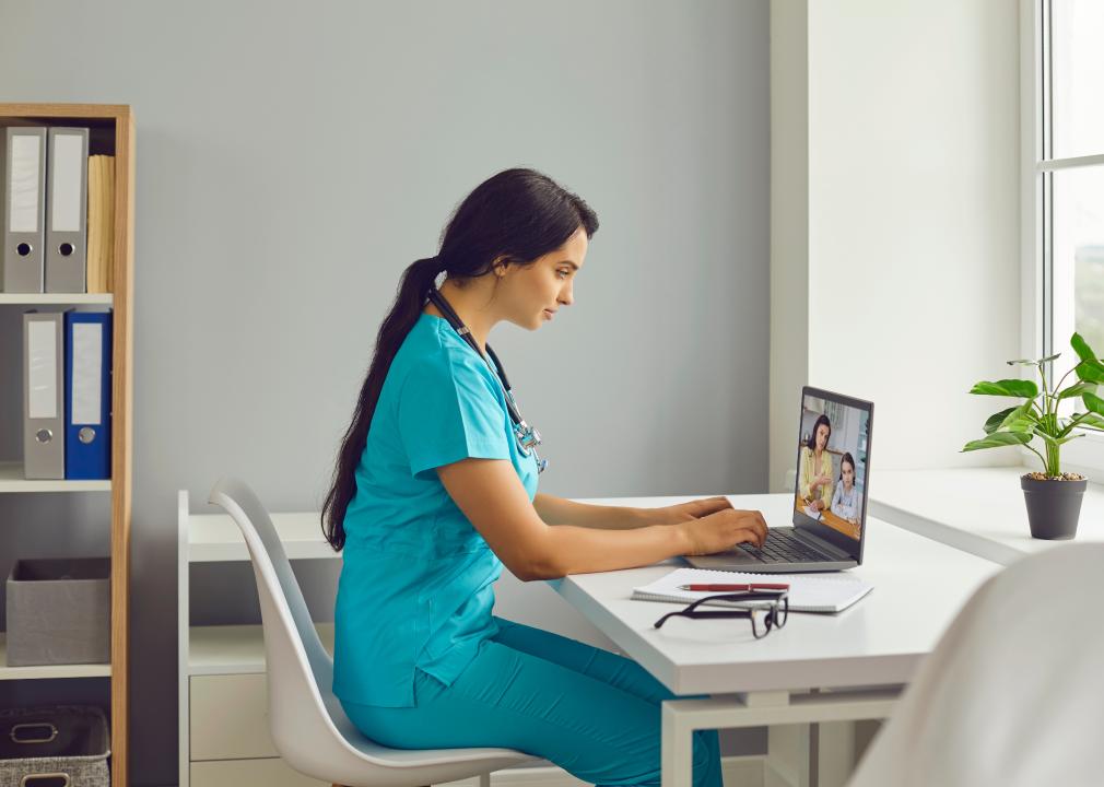 Young female nurse in blue scrubs with a stethoscope gives an online consultation.