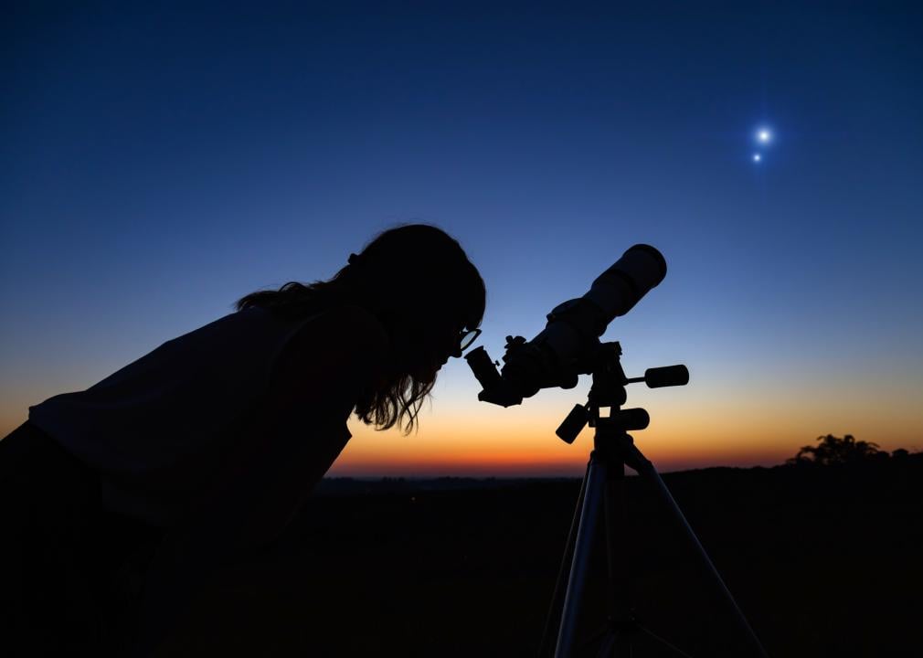 A silhouette of a person looking at the night sky with an astronomical telescope.