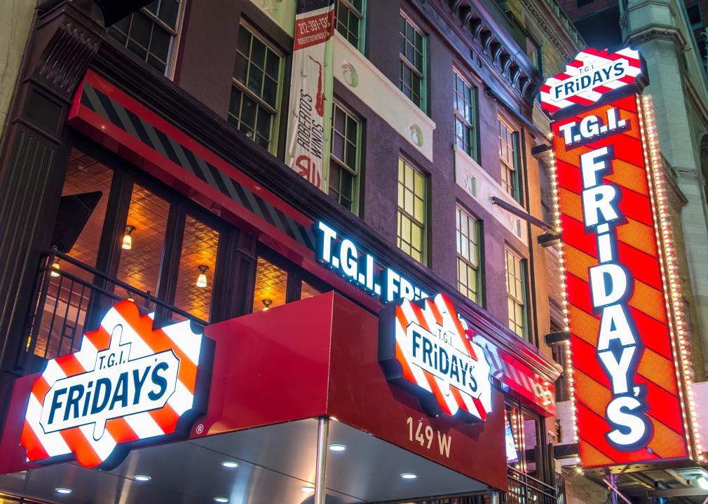 A brightly lit TGI Fridays on the ground level of a tall brick building.