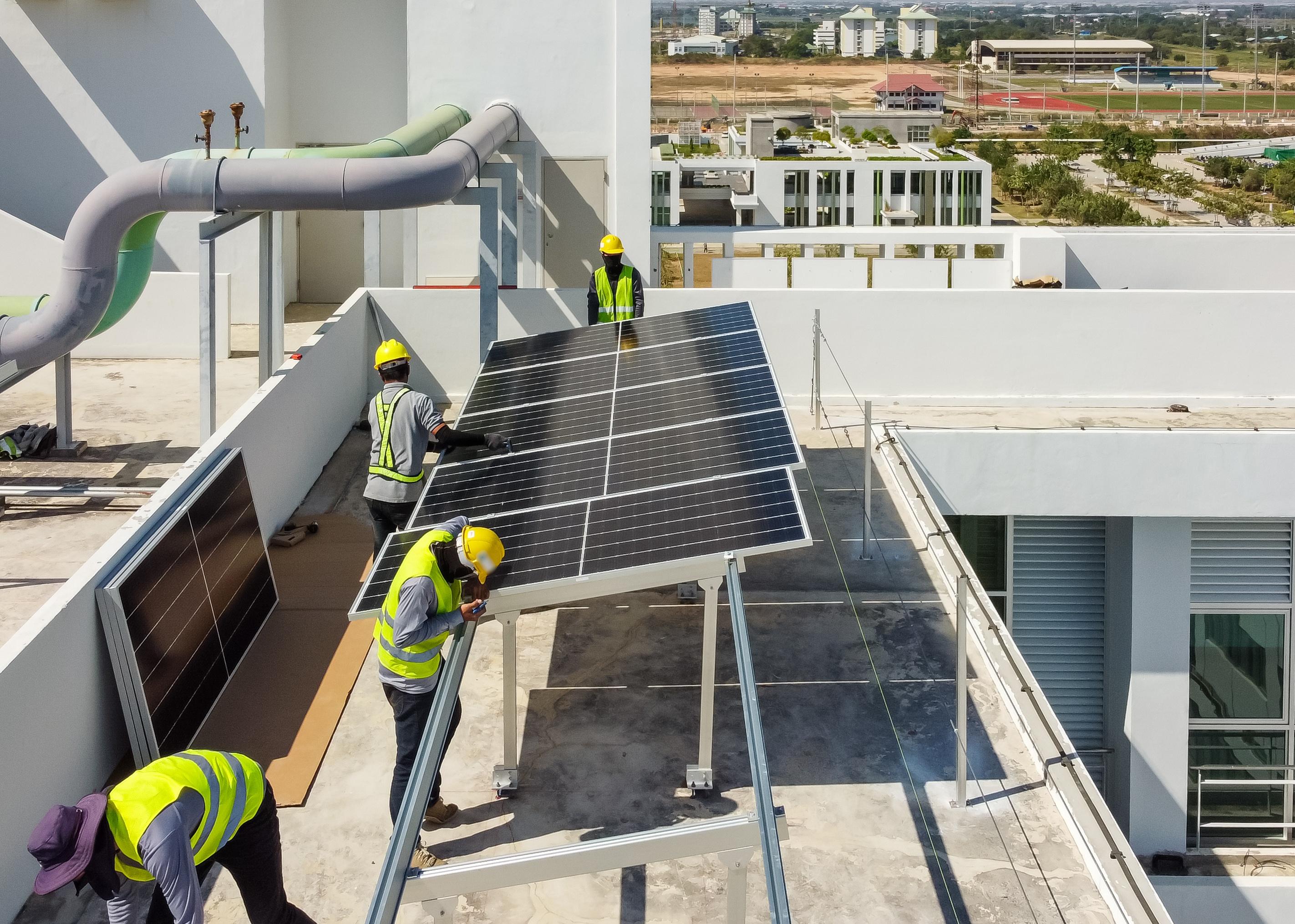 Workers installing solar panels on roof of a large industrial building