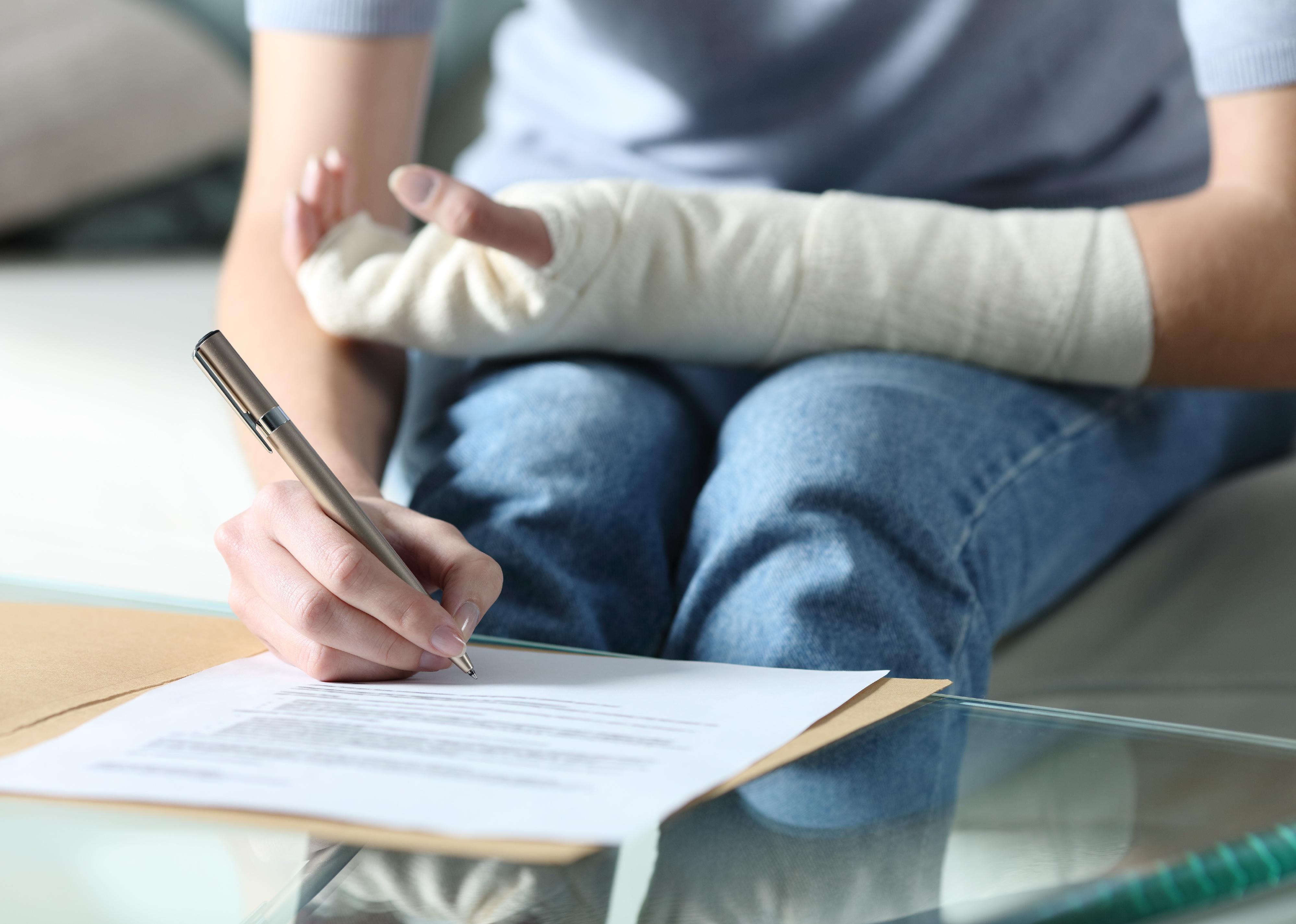 Close up portrait of a person with bandaged arm signing insurance document.