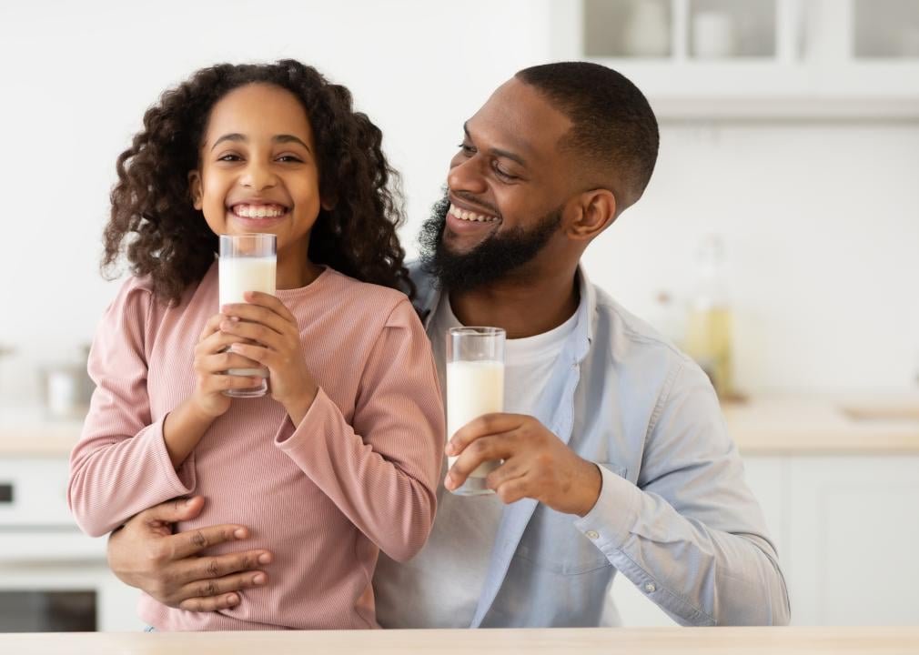 Smiling girl holding glass and drinking milk with her father in the kitchen.