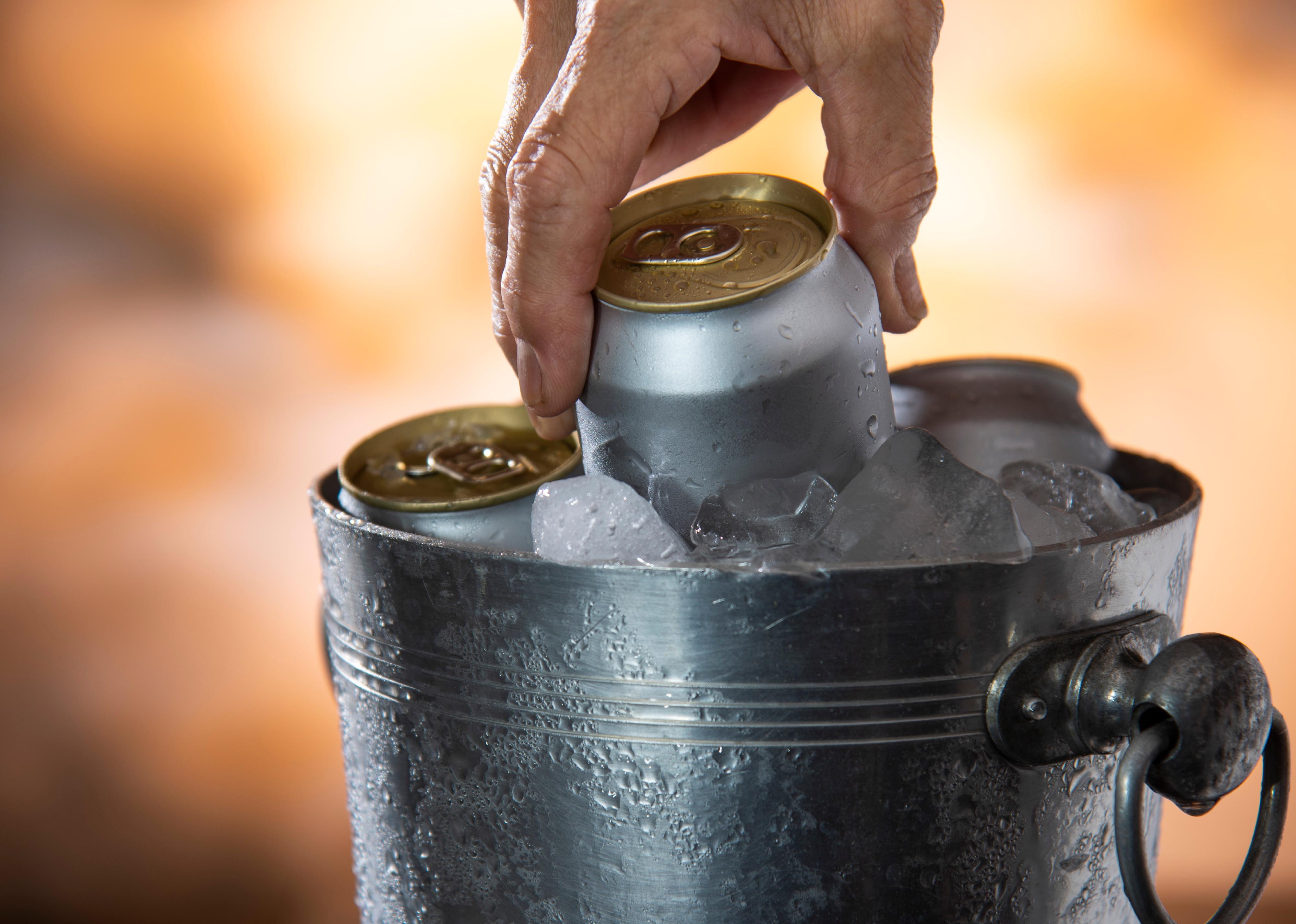 Hand picking cold beer can from ice cooler