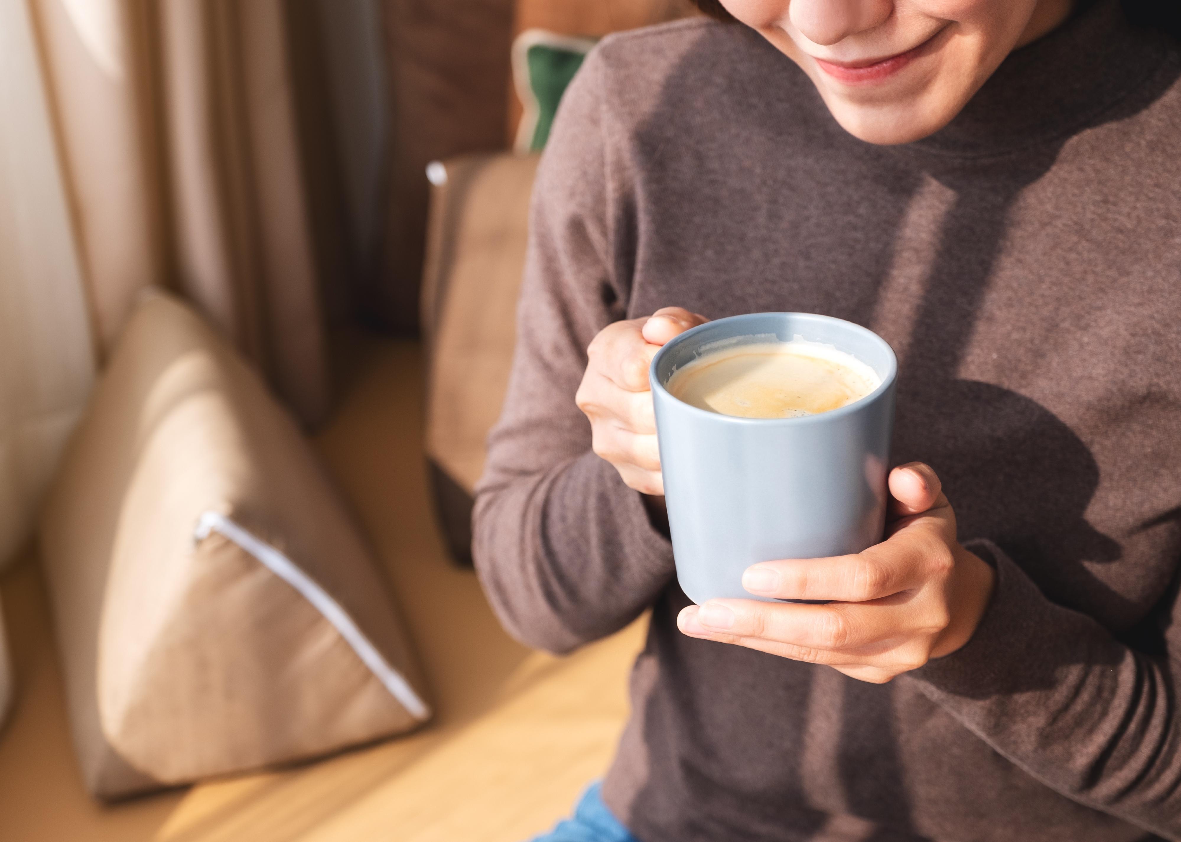 Closeup image of a young woman drinking hot coffee at home in the morning.