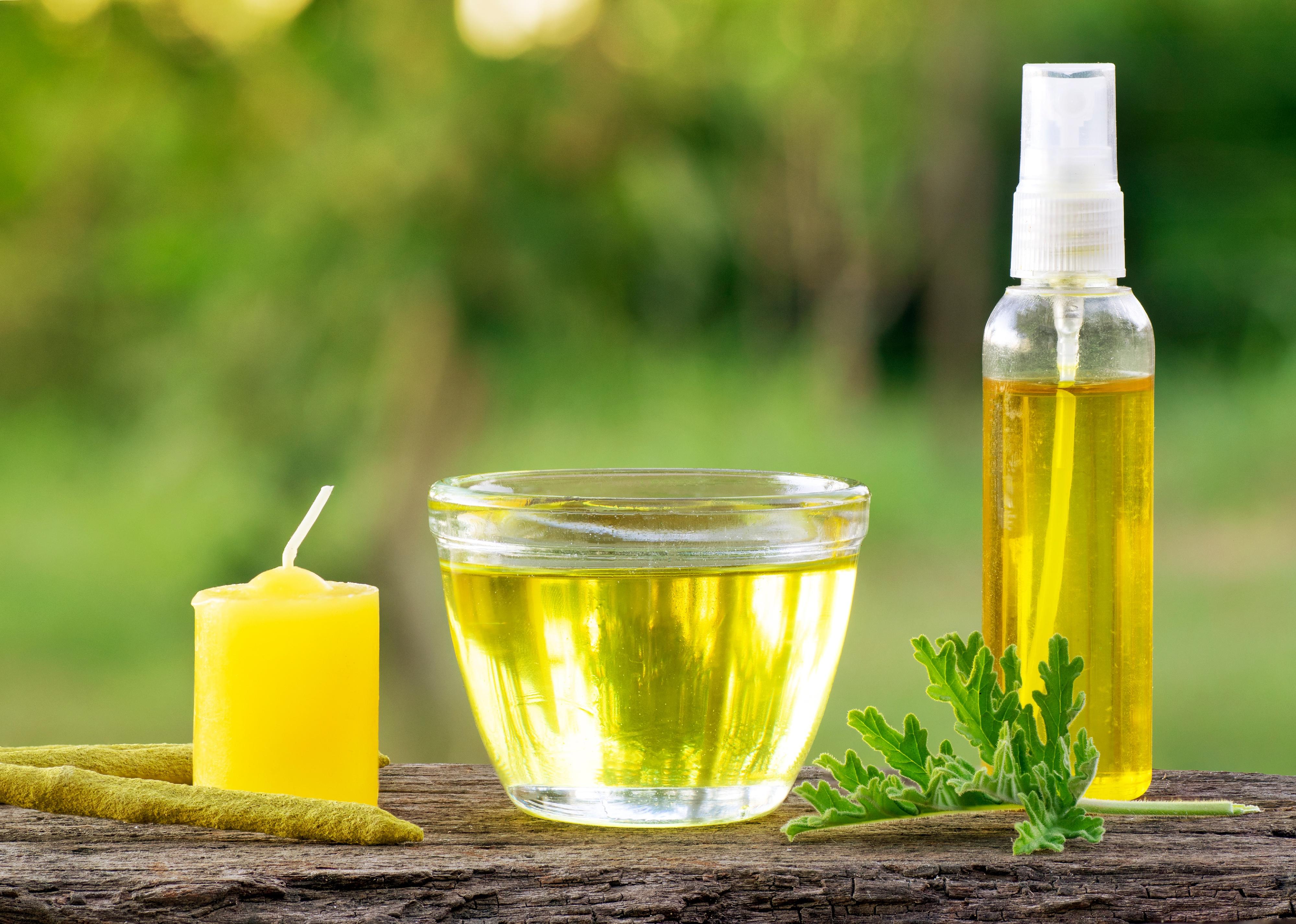 Citronella oil in a cup with a candle, incense, and spray bottle.