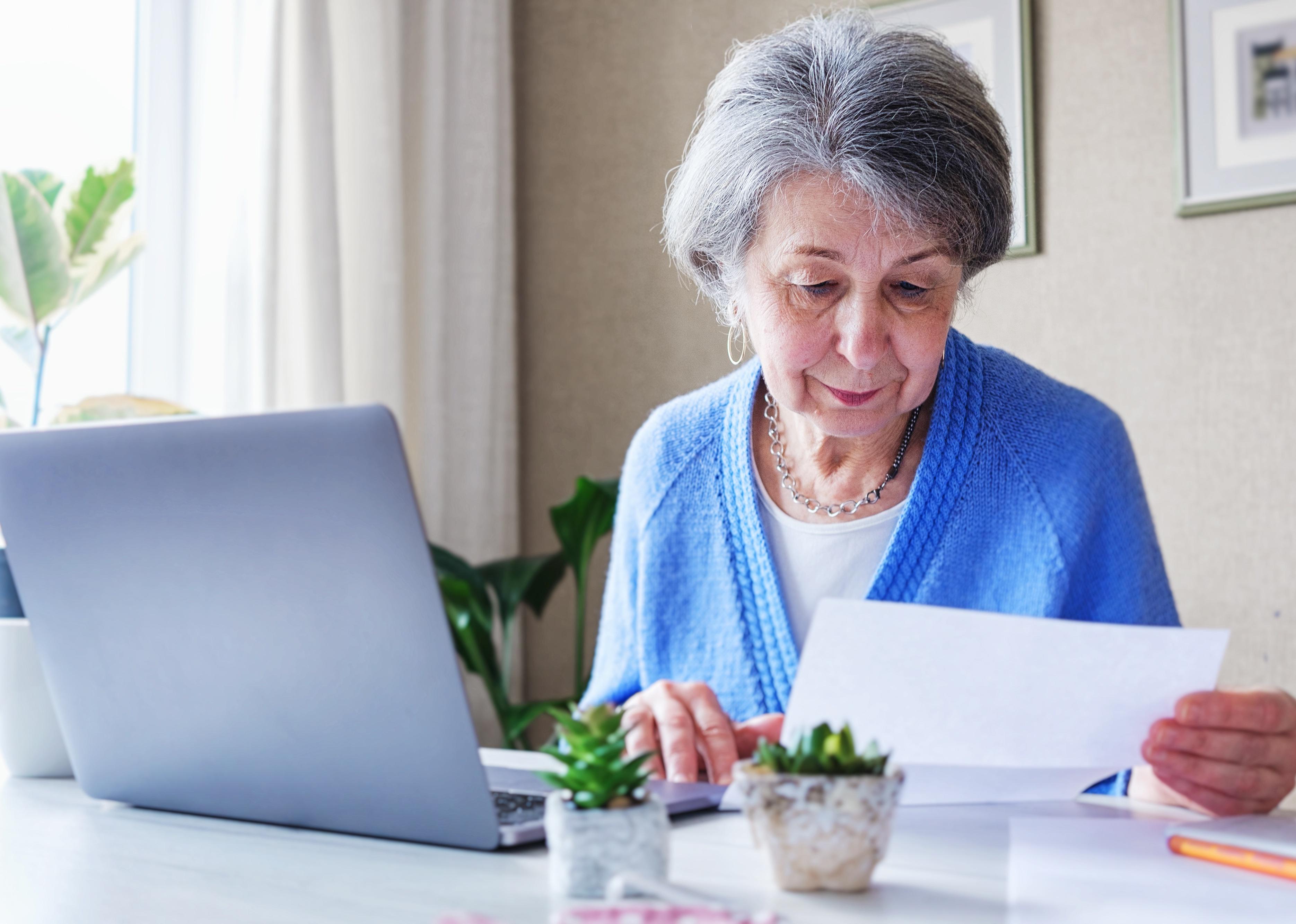Elderly person reads a printed letter, sitting at a desk.
