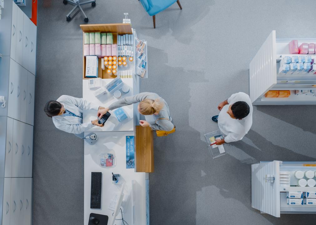 An aerial view of a pharmacy checkout counter with a pharmacist and customer interacting.