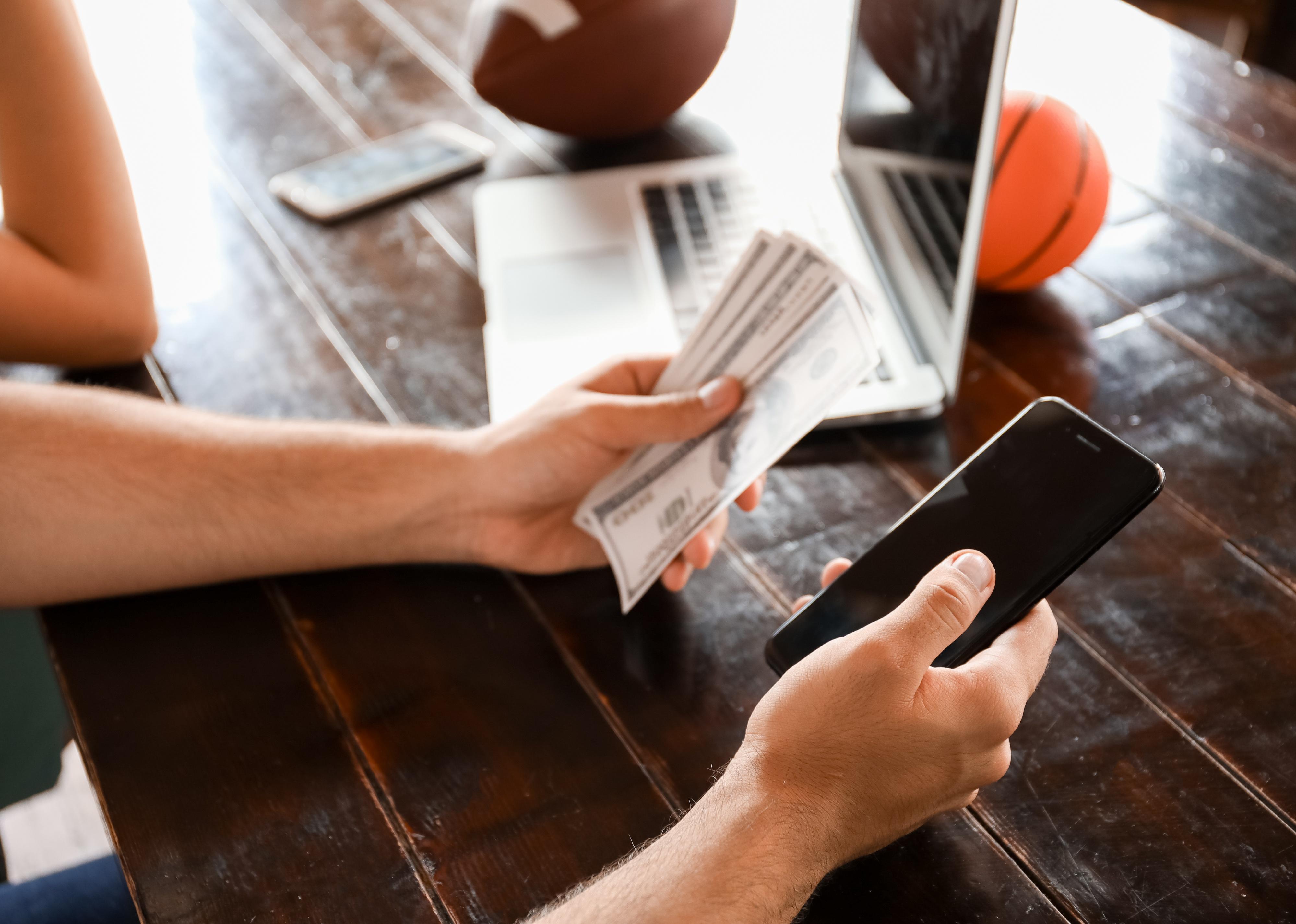 Young man with money and mobile phone placing sports bet.