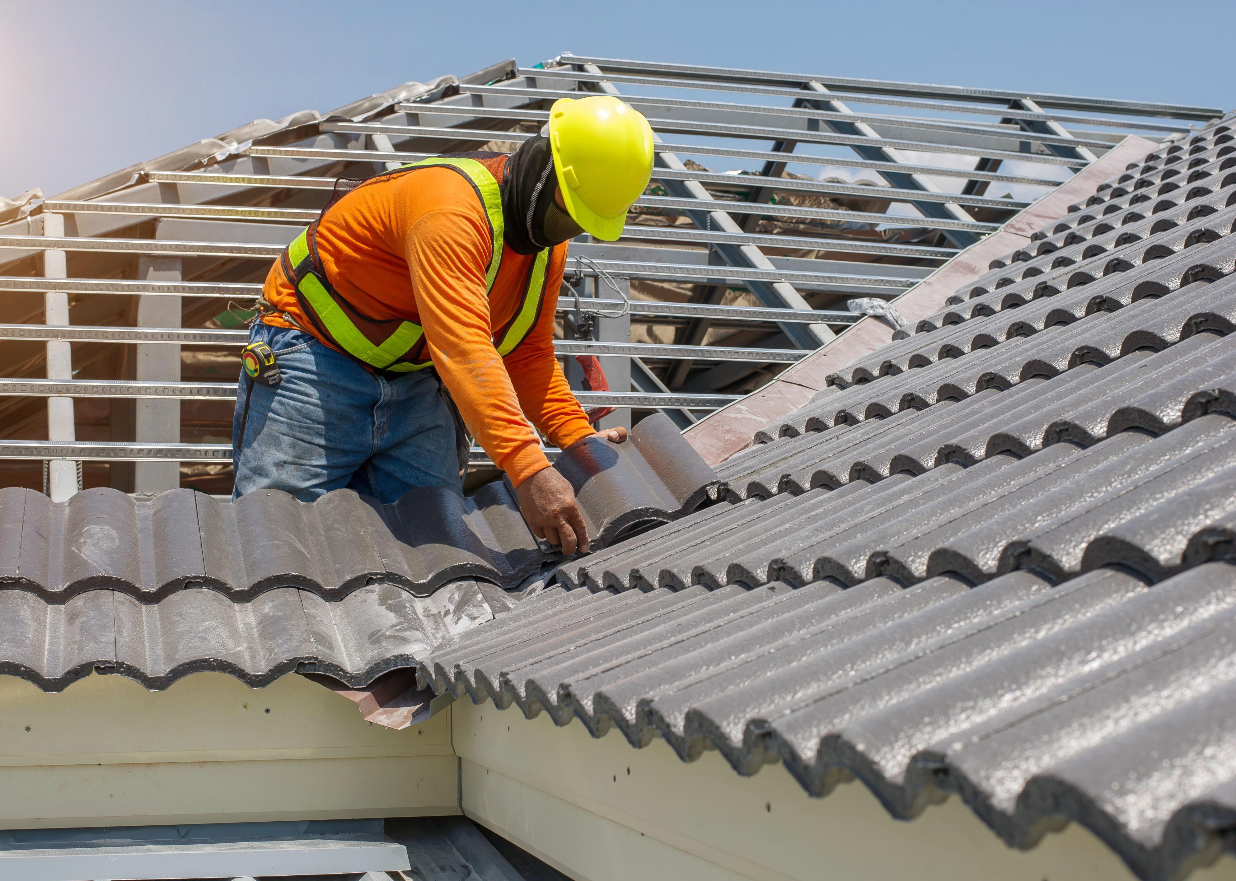 Worker with white gloves replacing gray shingles on house.