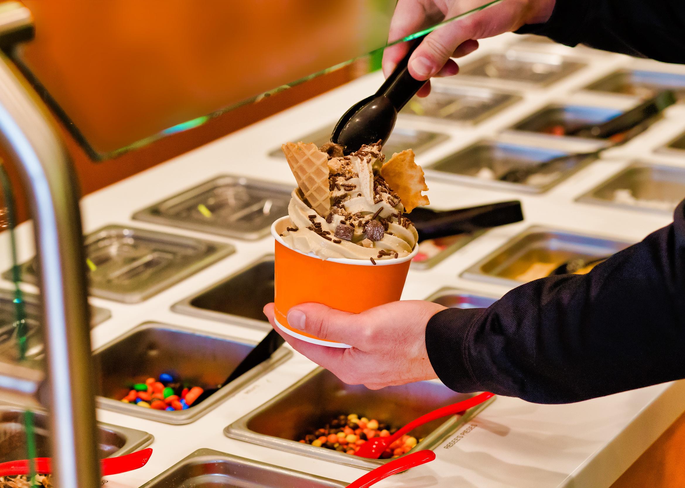 Hand building frozen yogurt with chocolate chips and sprinkles at a buffet.