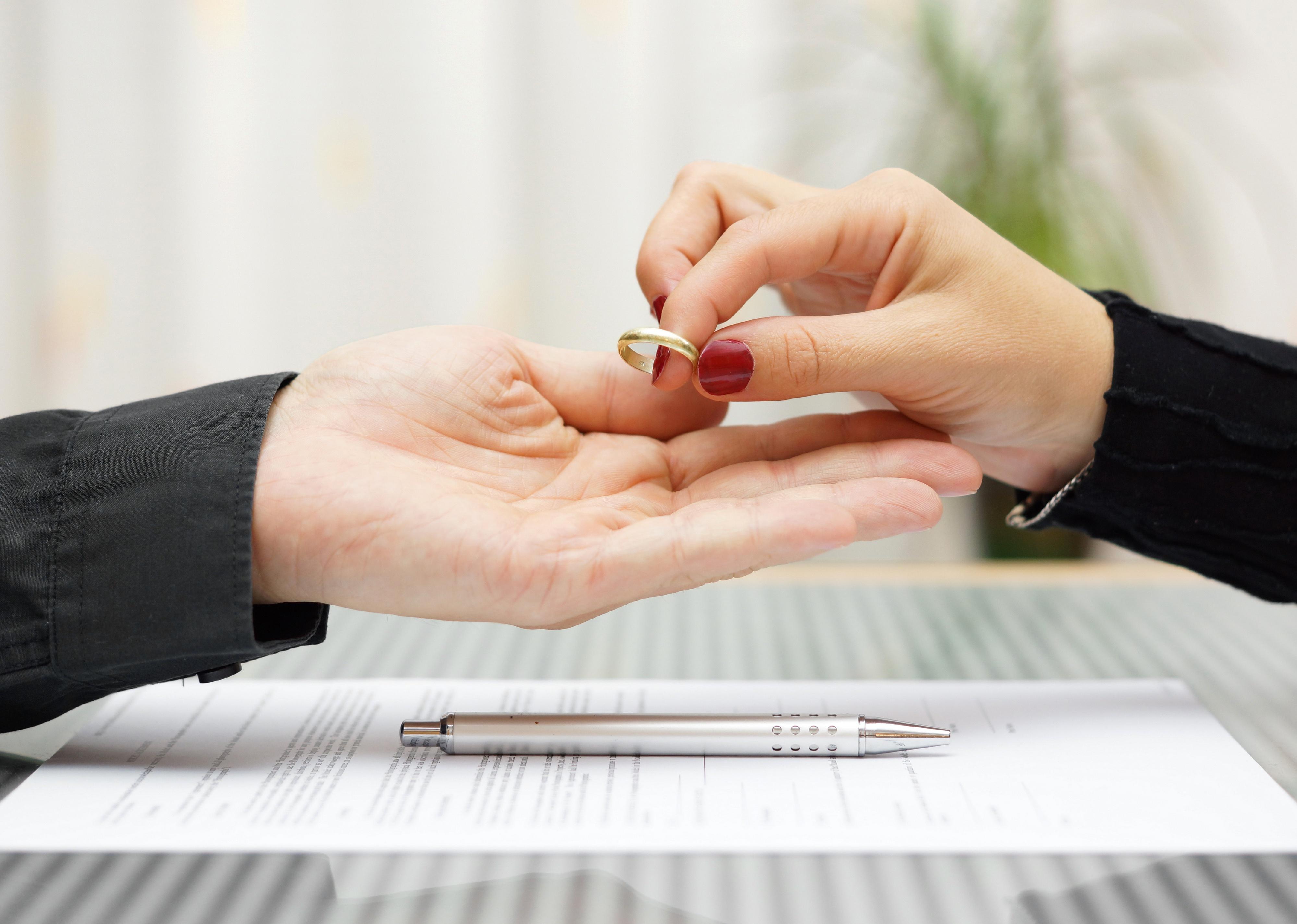 Hands passing ring over divorce papers.