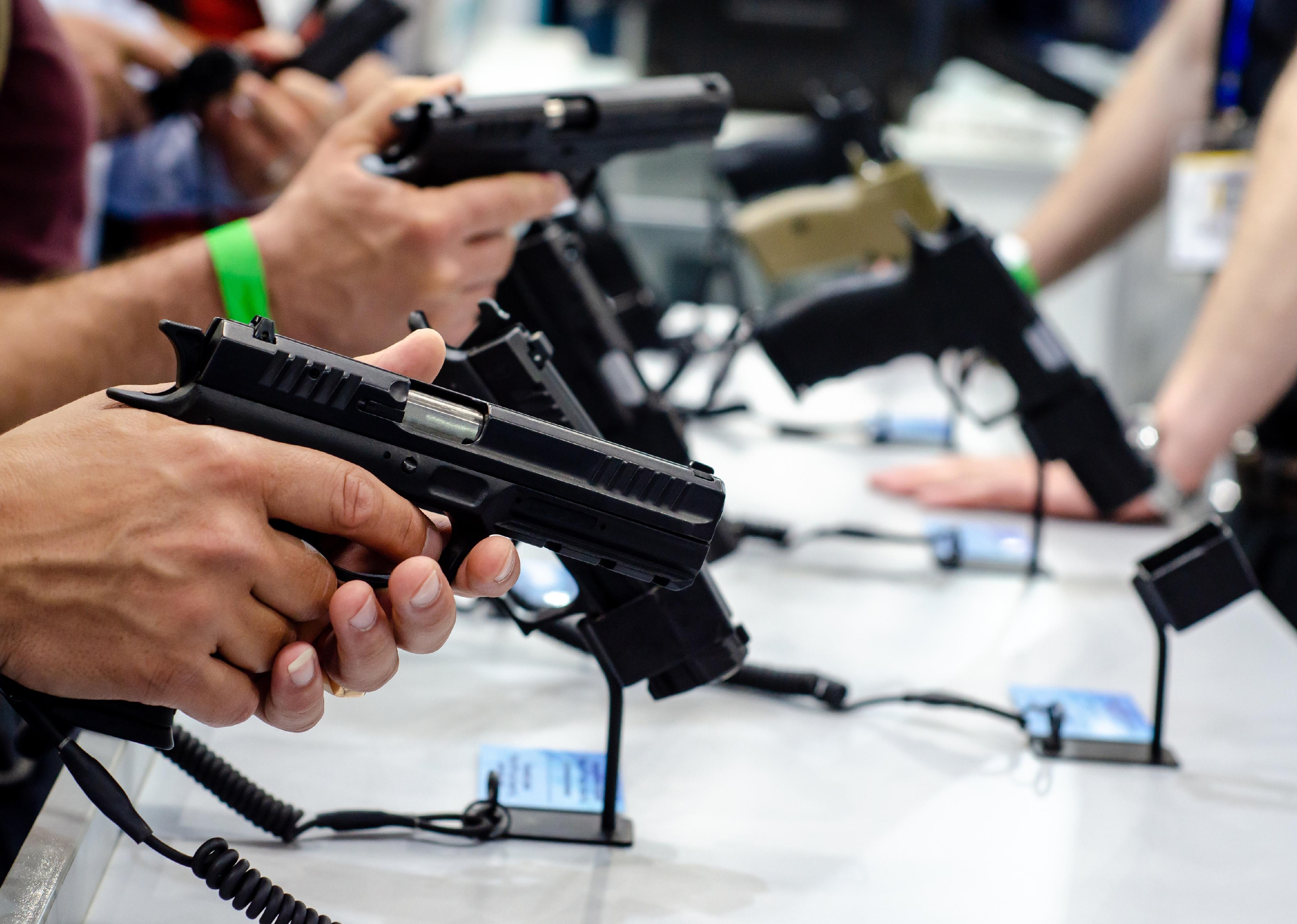 A row of hands holding guns in a store.