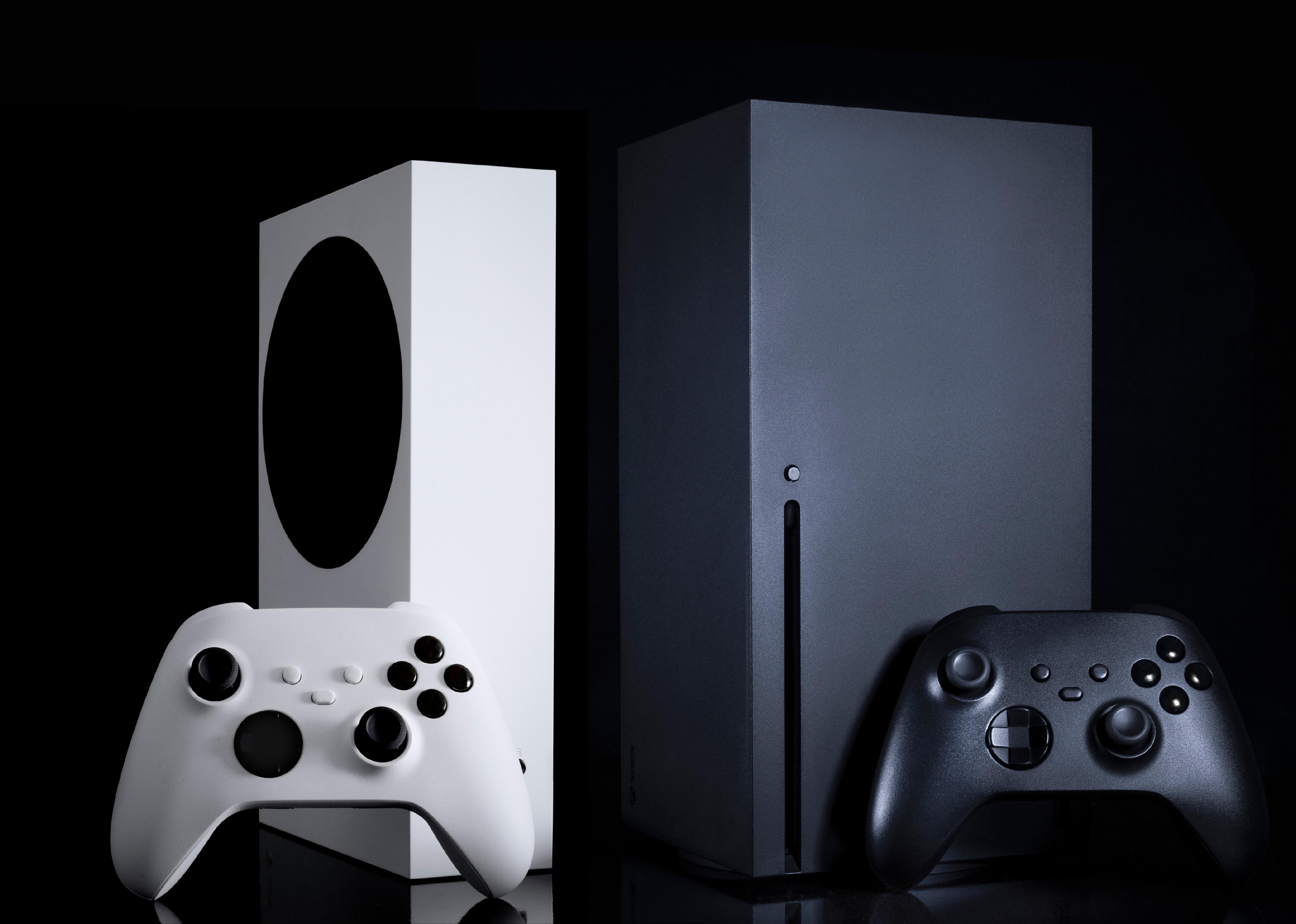 White and black game consoles and controllers with black background.