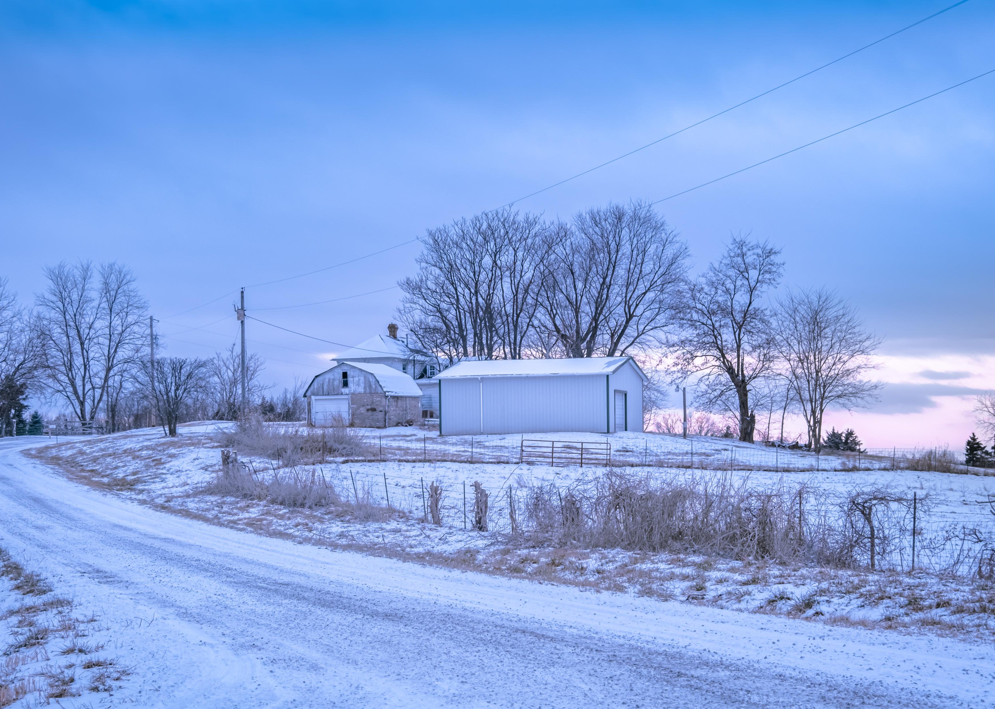 View of rural Midwestern road in winter with distant farm buildings.