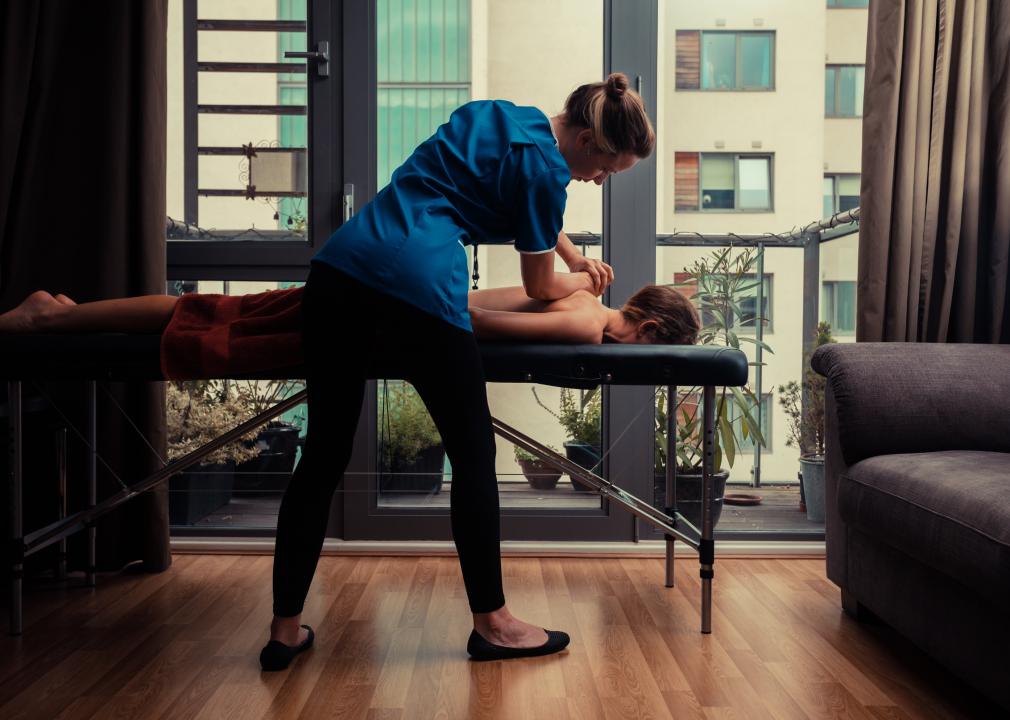 A massage therapist treating a client on a table in an apartment.
