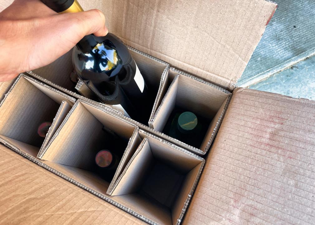 A hand taking a bottle of wine out of a delivery box.