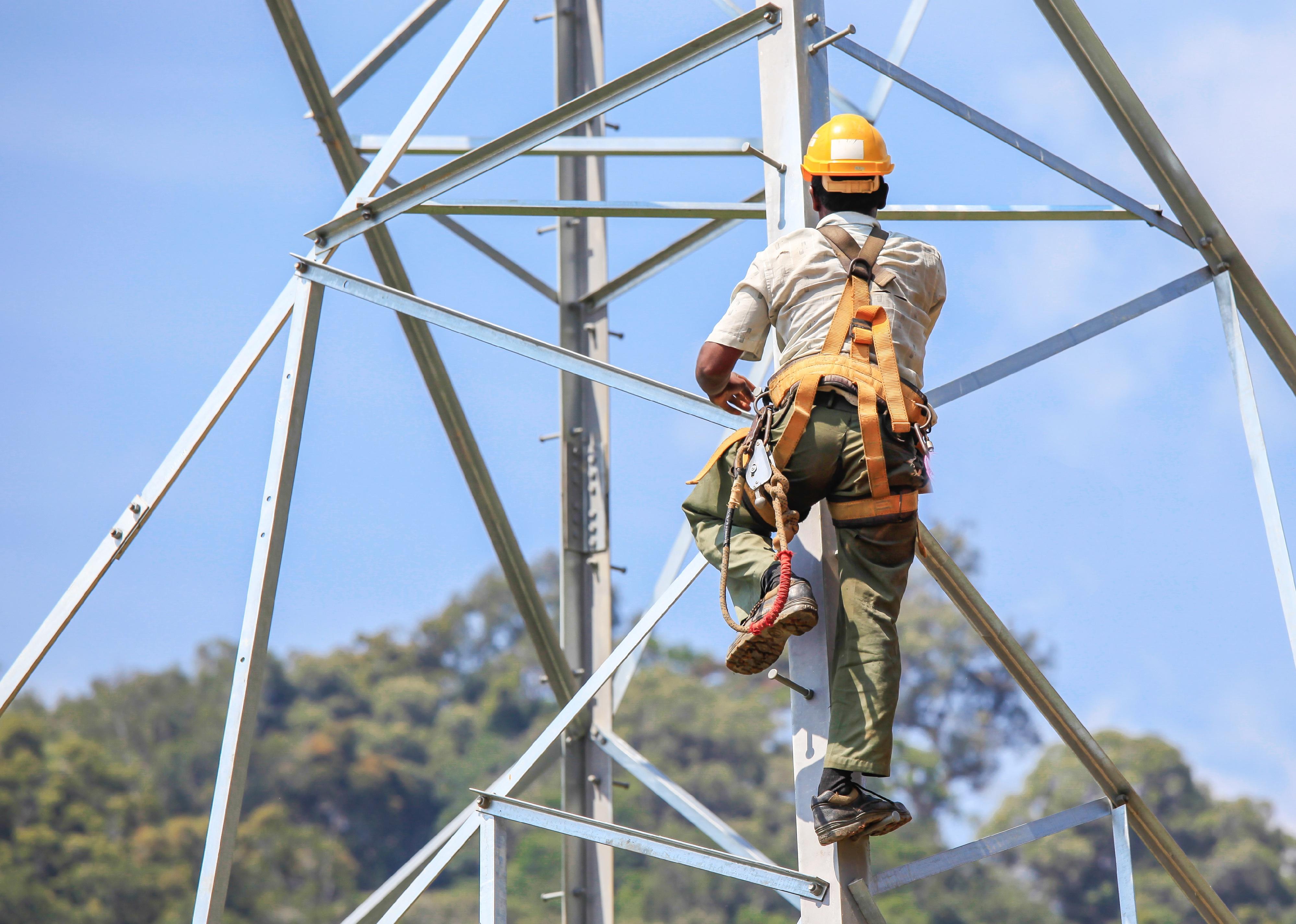 Worker climbing on transmission line tower.