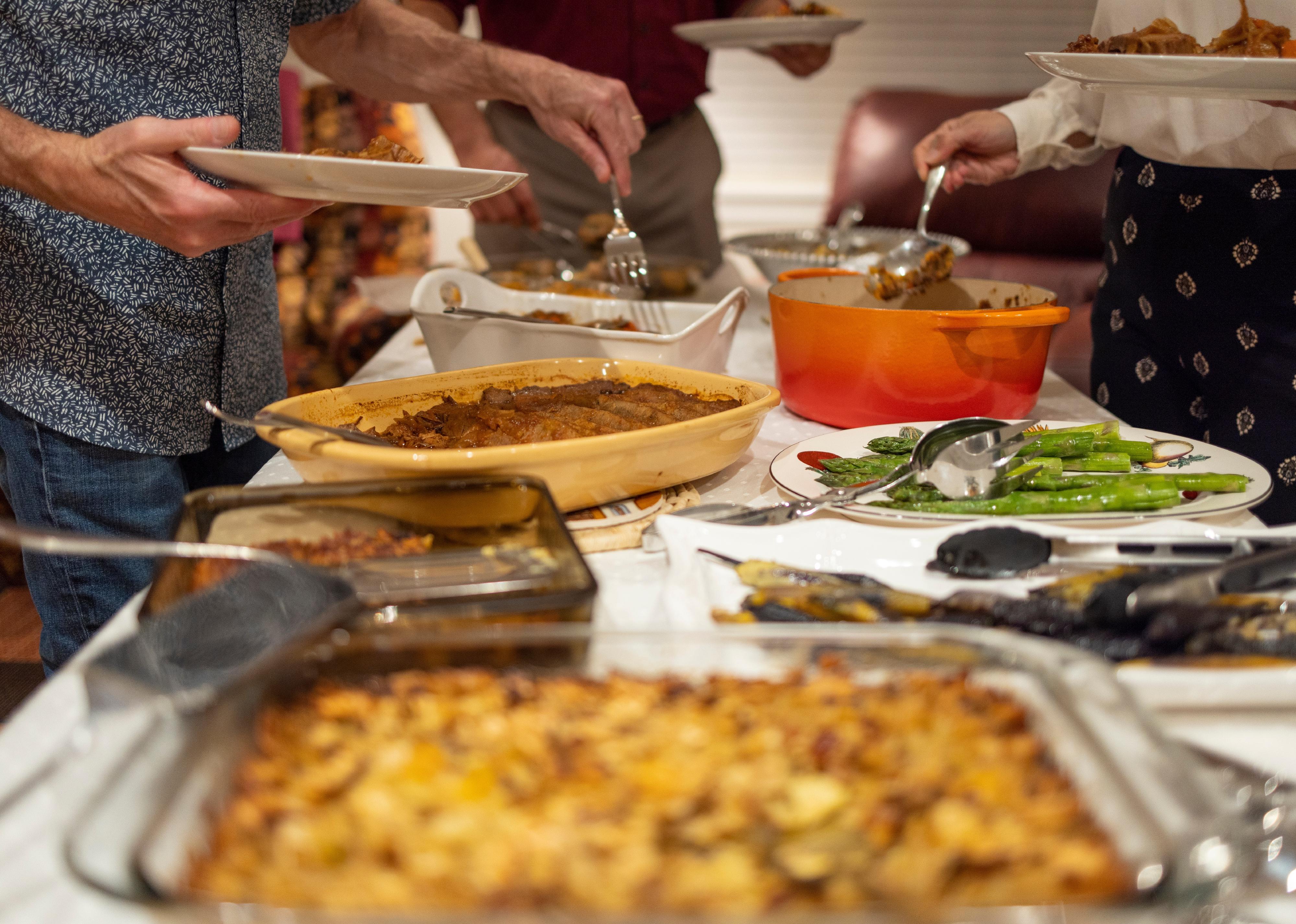 Potluck with people gathered around the food serving themselves dinner.