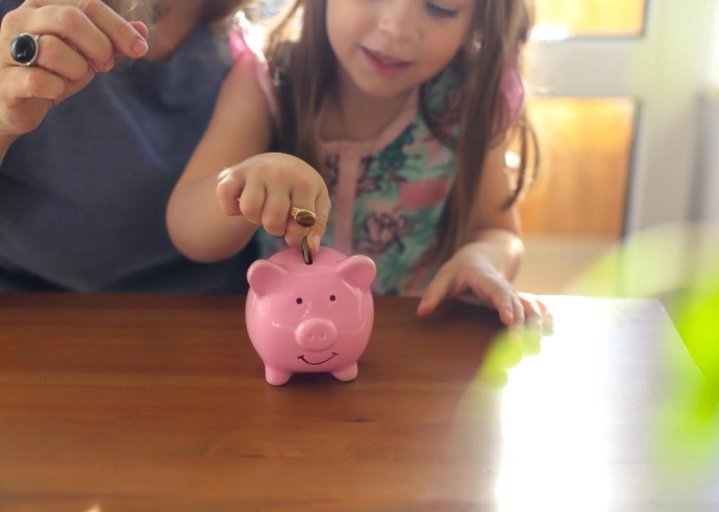 A young girl drops a coin into a pink piggy bank. 